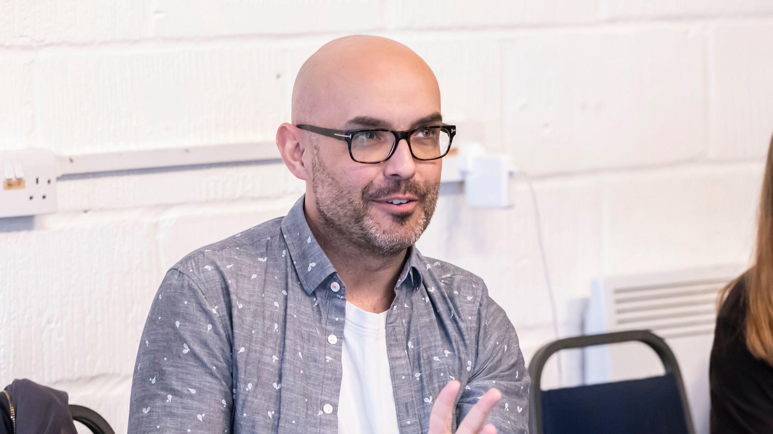 A bald man wearing glasses and a blue shirt