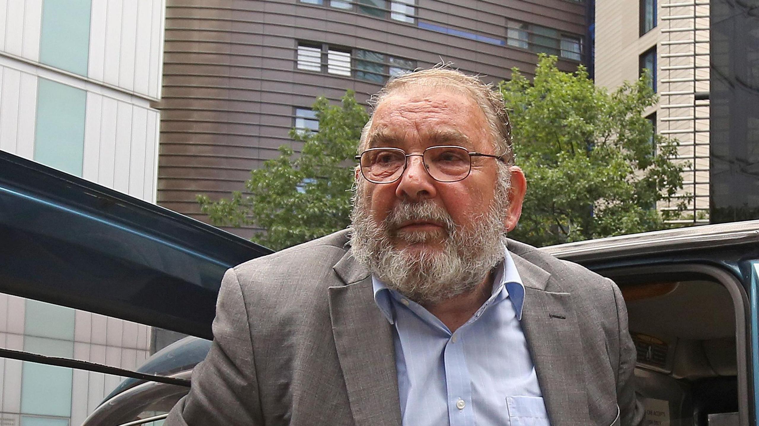 Lord Hanningfield. He has a grey and white beard, he is wearing glasses, a grey suit and blue shirt. He is getting out of a black taxi. 