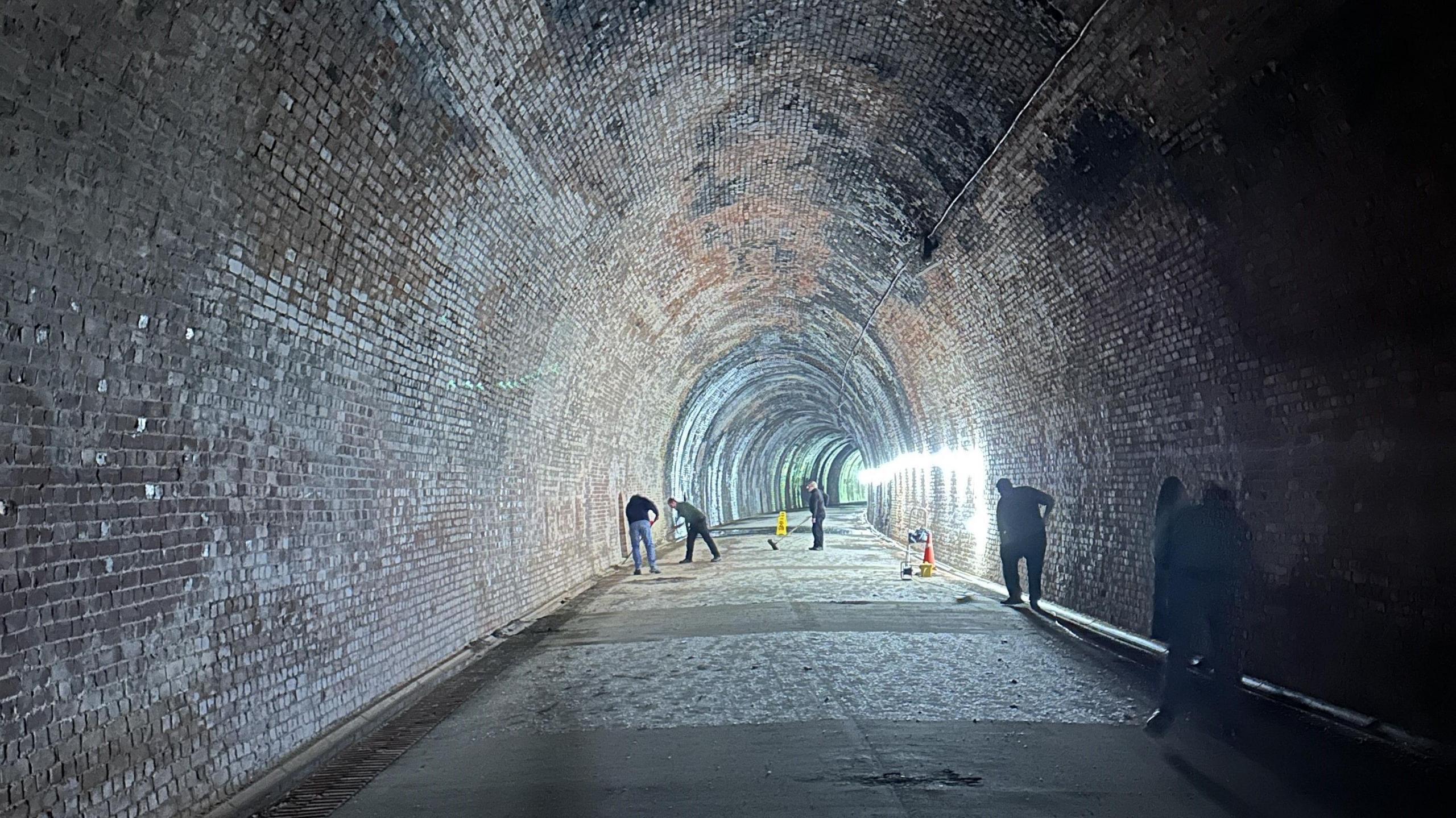 A long brick tunnel with people in the distance sweeping the ground.