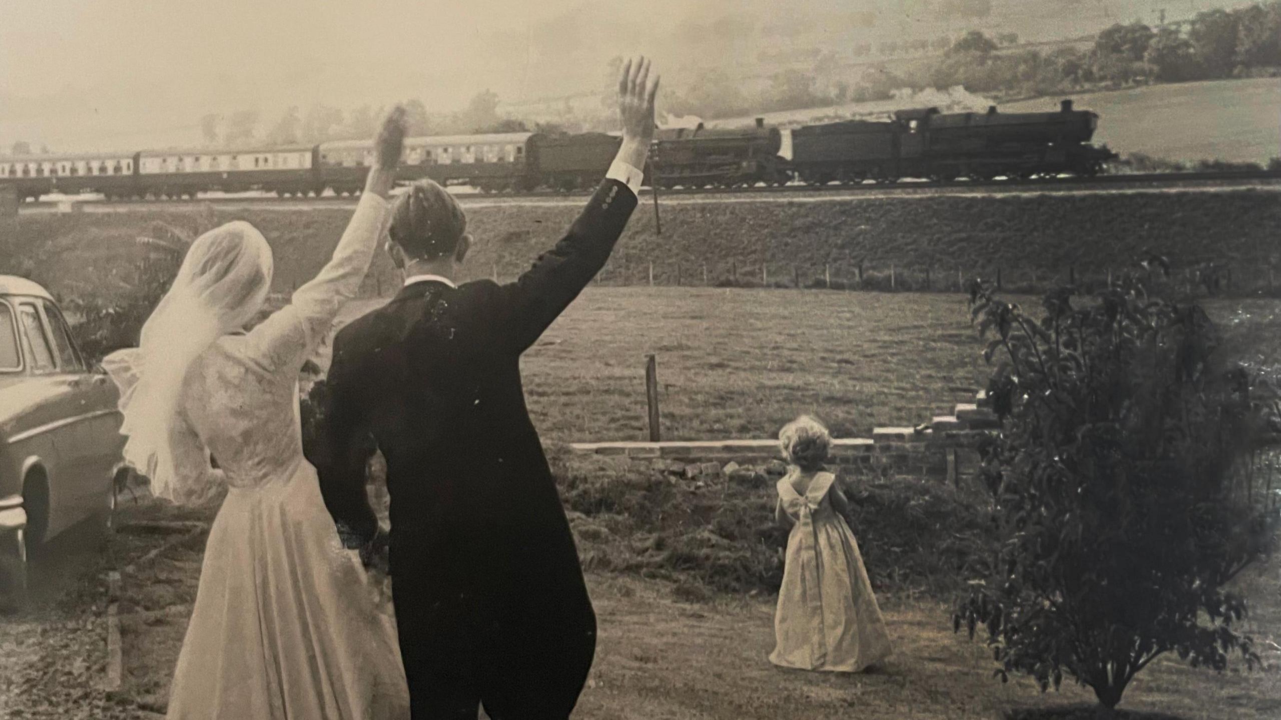 Image shows Margaret and George on their wedding day waving to a stream train passing by