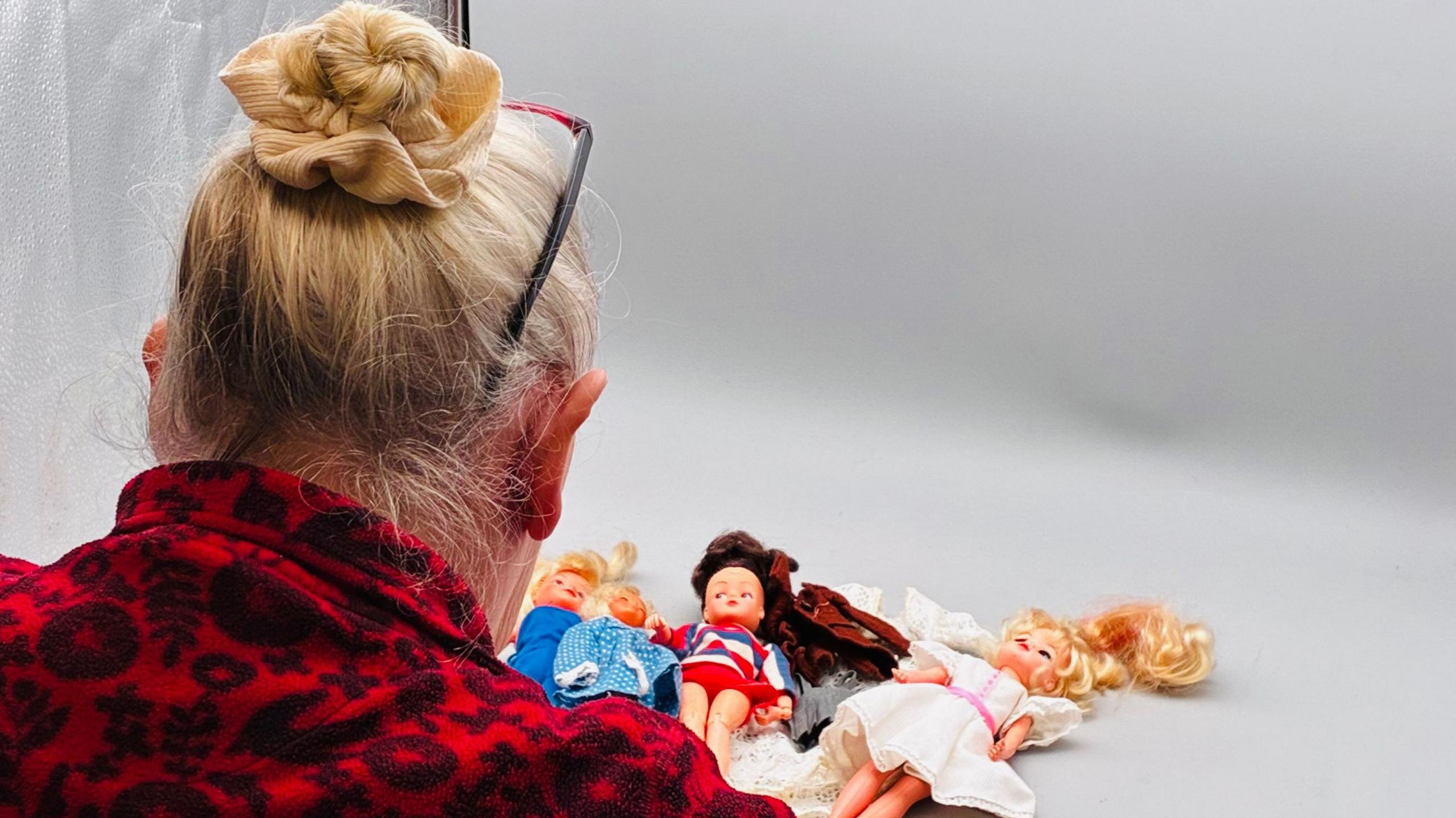 Jay Boydon with her back to the camera. Several dolls are laid in front of her.