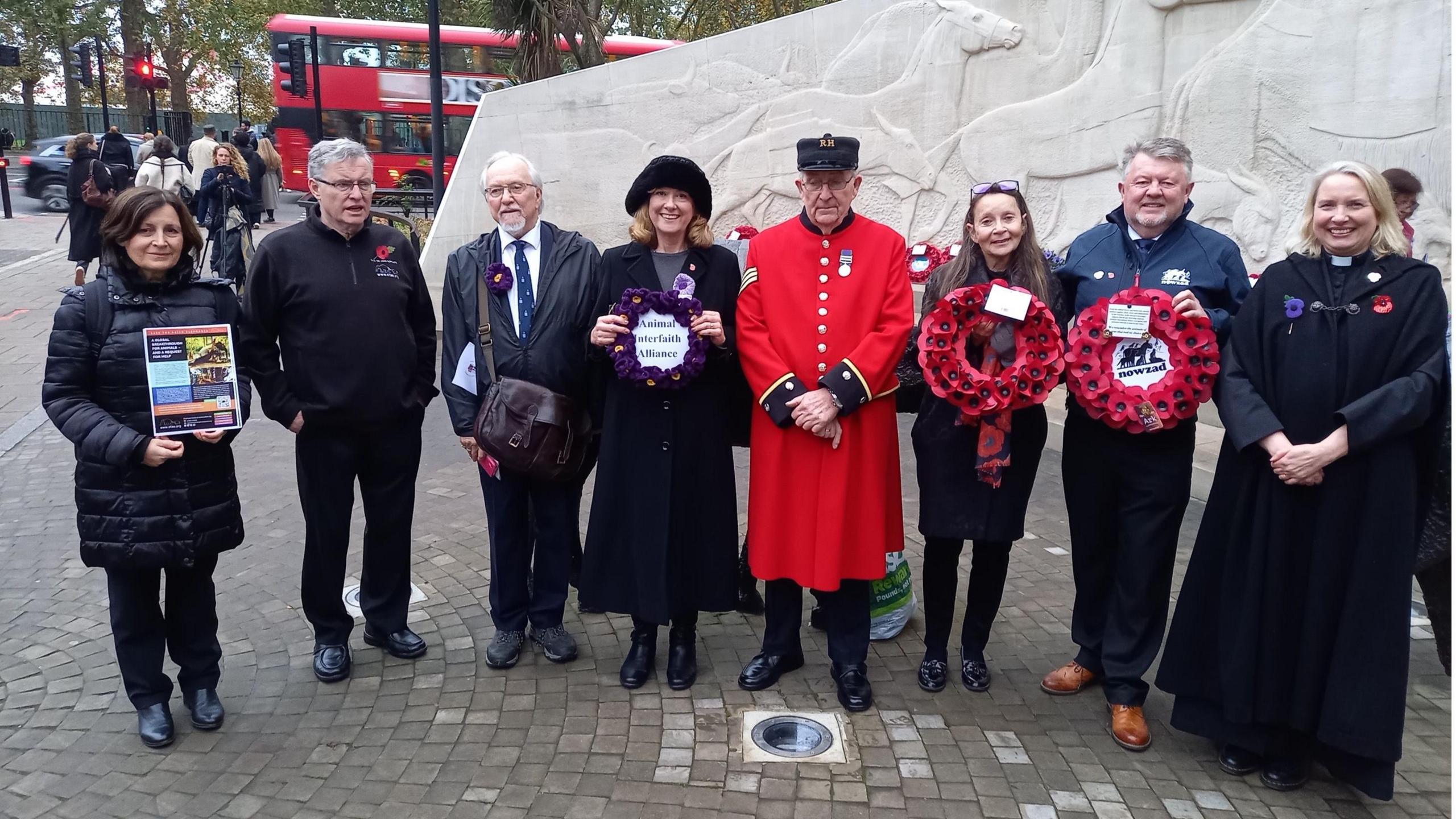 A picture of 8 people in a line standining holding wreaths alongside posters