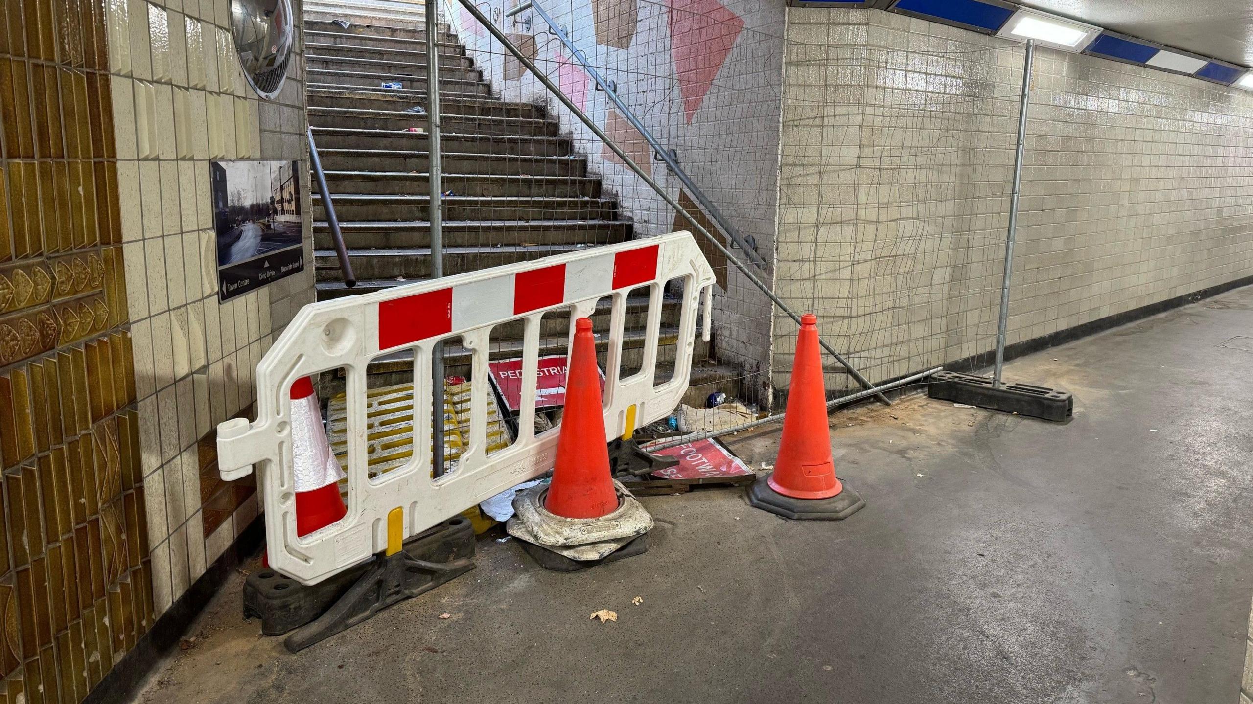 Cones and a plastic barrier block a stairwell in the underpass