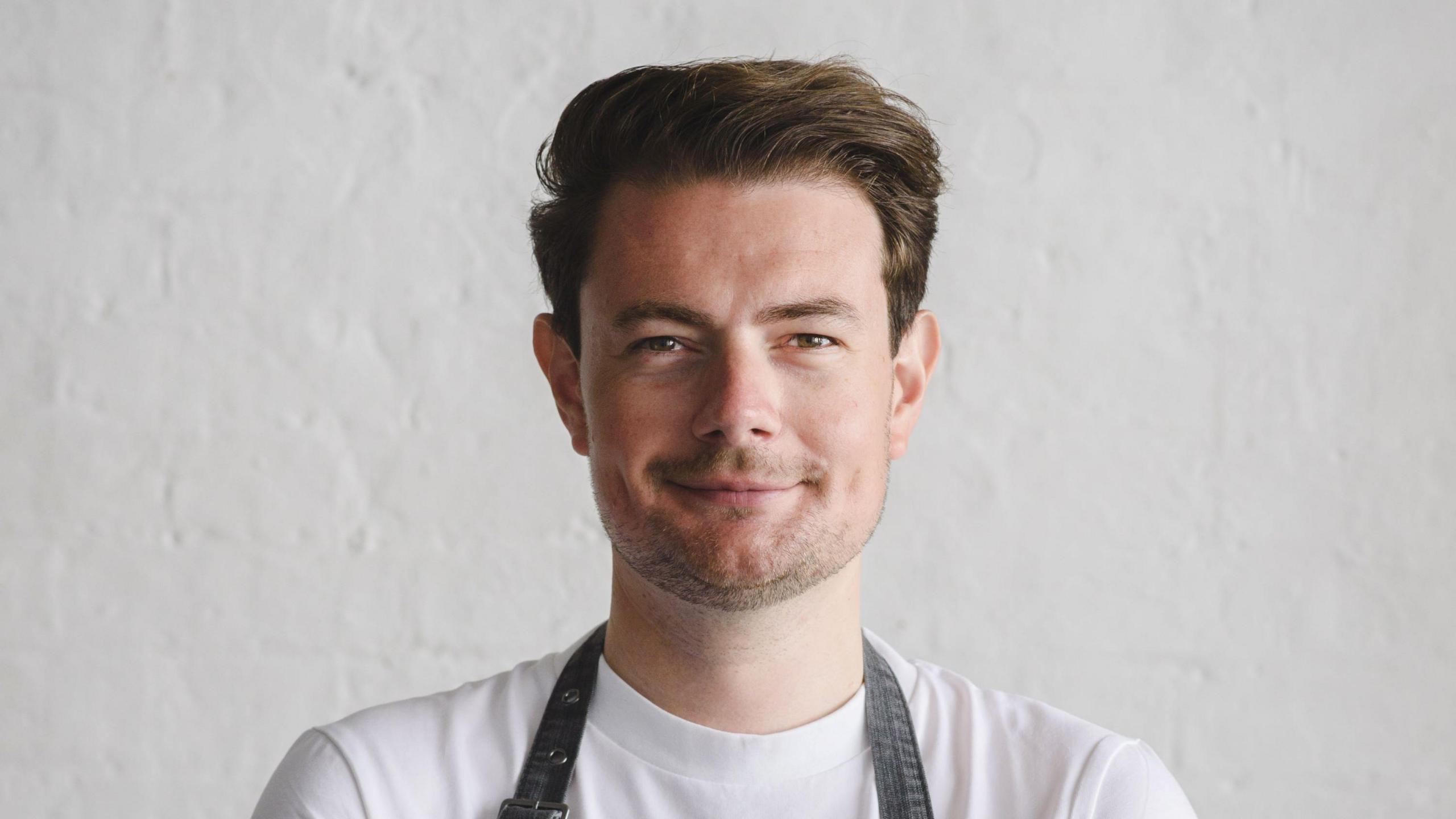 Head and shoulders shot of Thomas Frake in a white t-shirt and dark apron