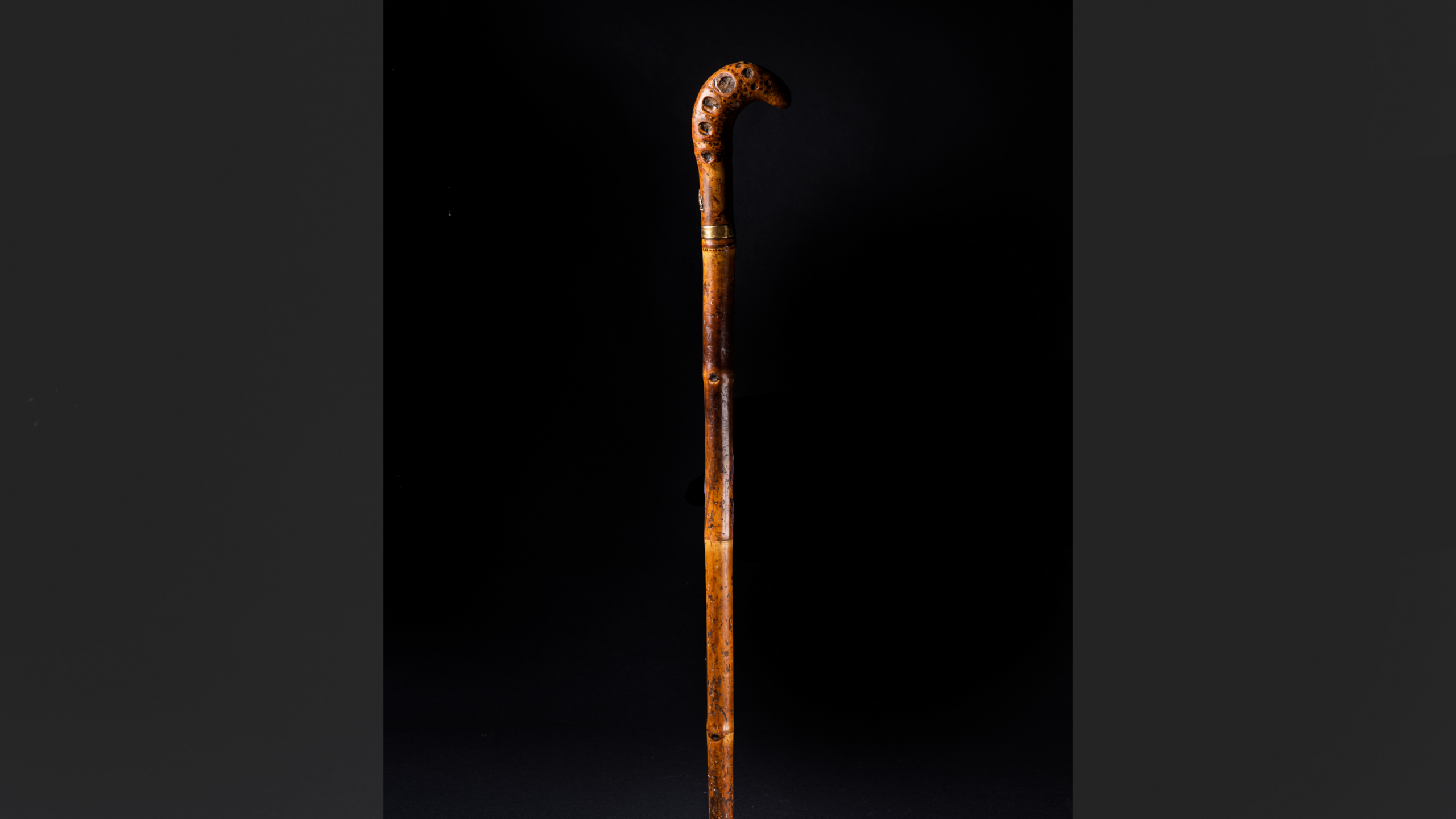 An ornate wooden walking stick against a black backdrop