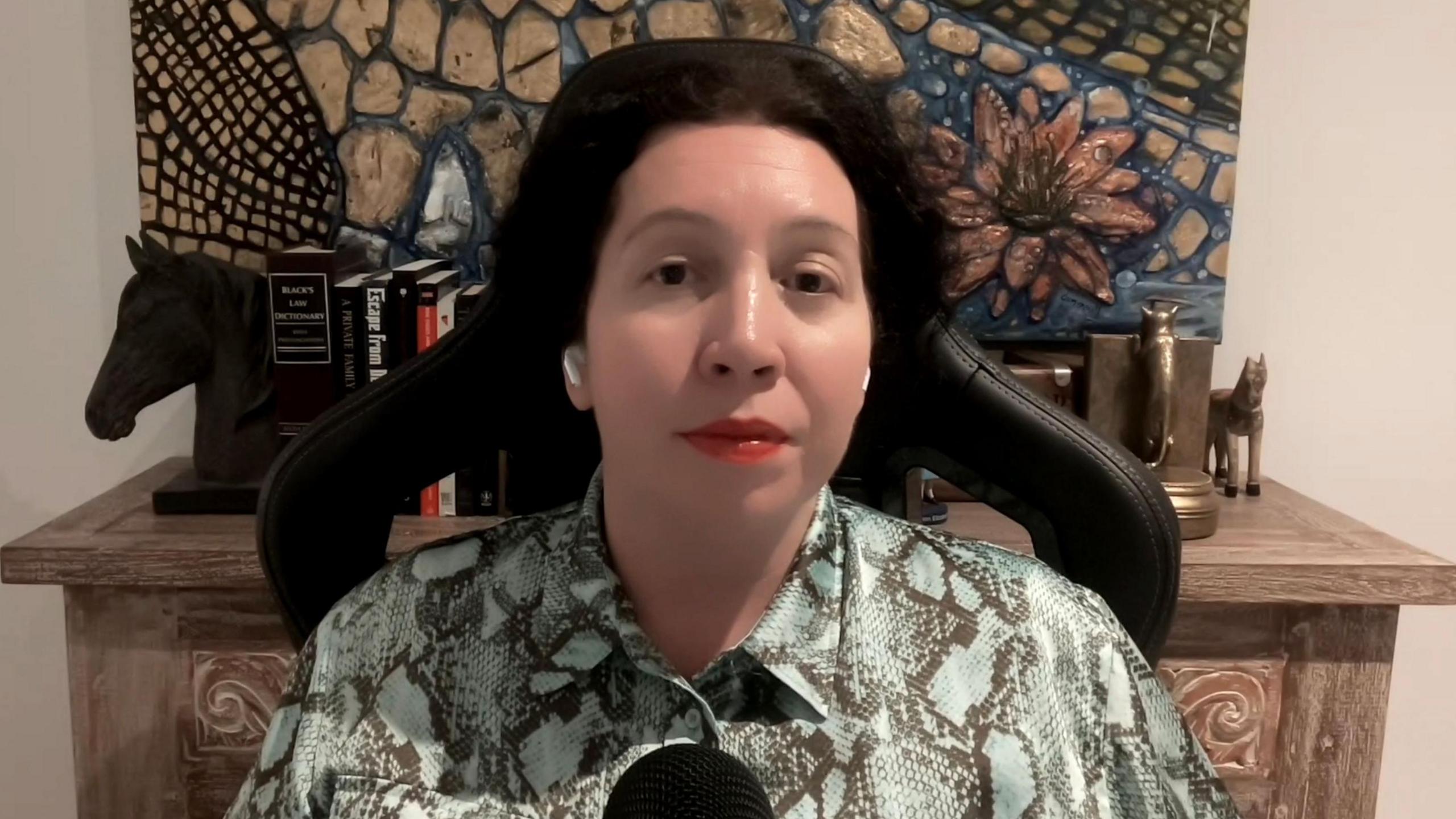 Radha Stirling, in a green printed shirt, sitting in a chair looking at the camera