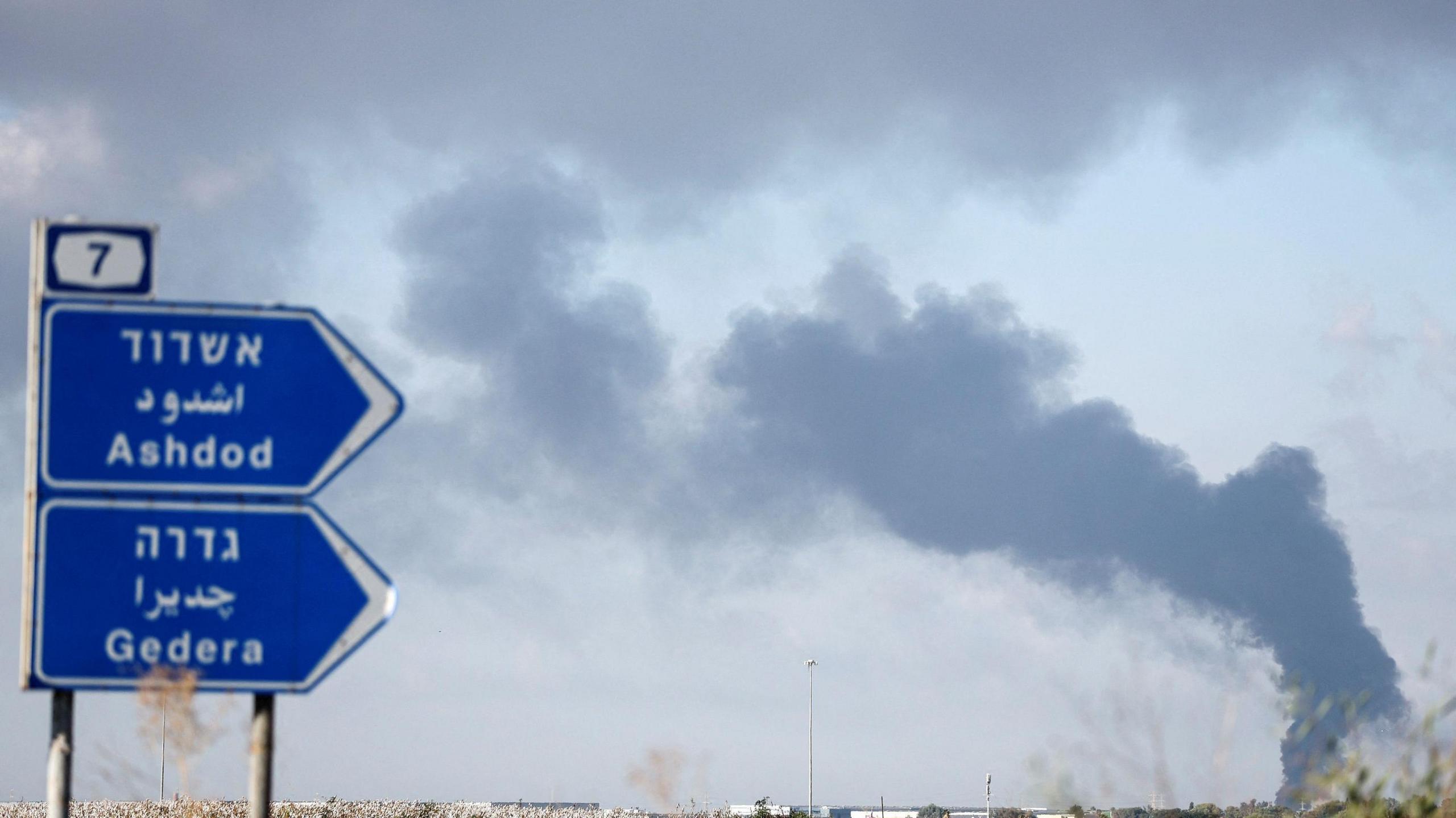 A blue finger signpost which points towards Ashdod and Gedera, where smoke is rising from the area.