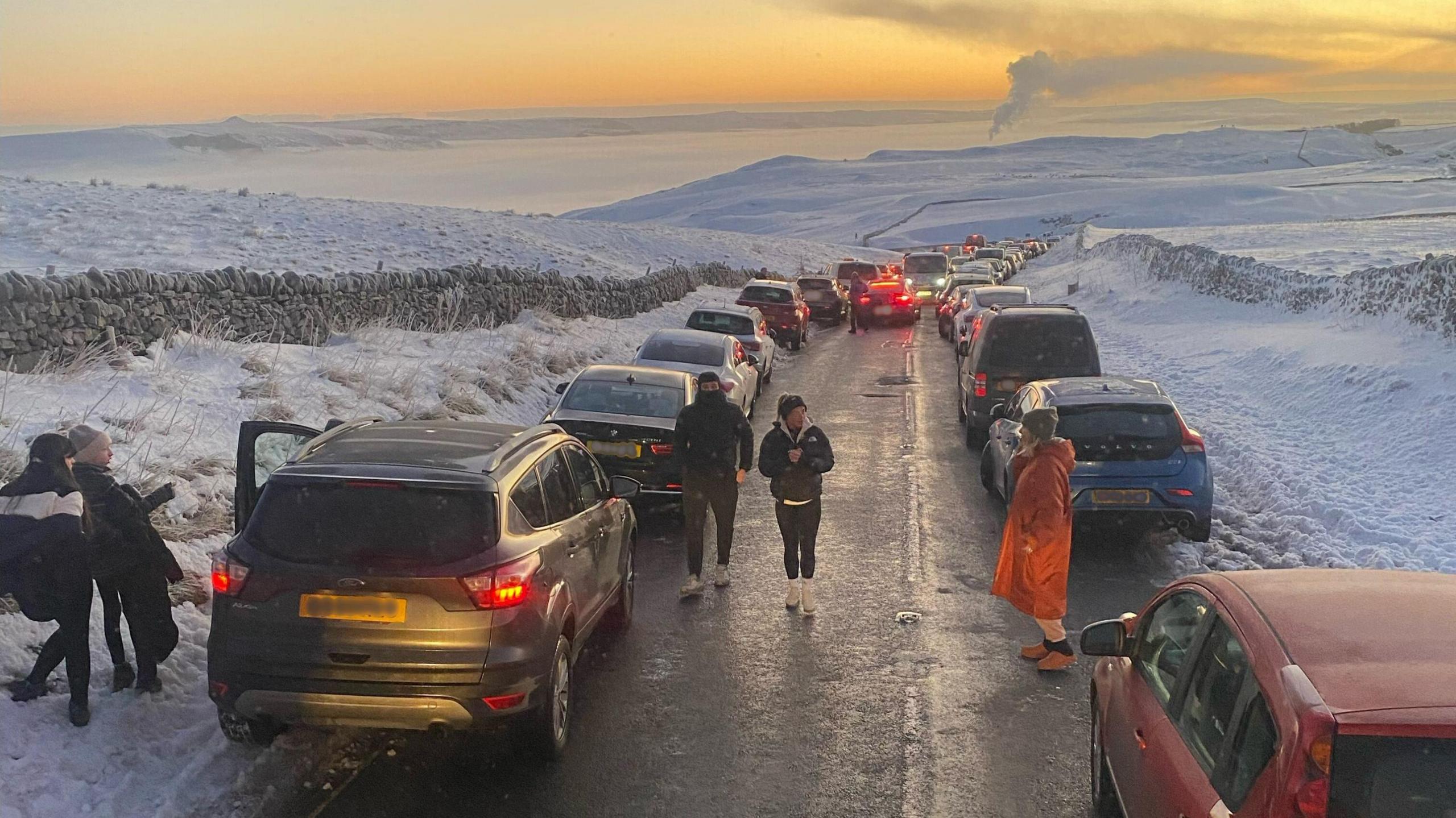 Rows of cars on both sides of a road high up in a snowy Peak District