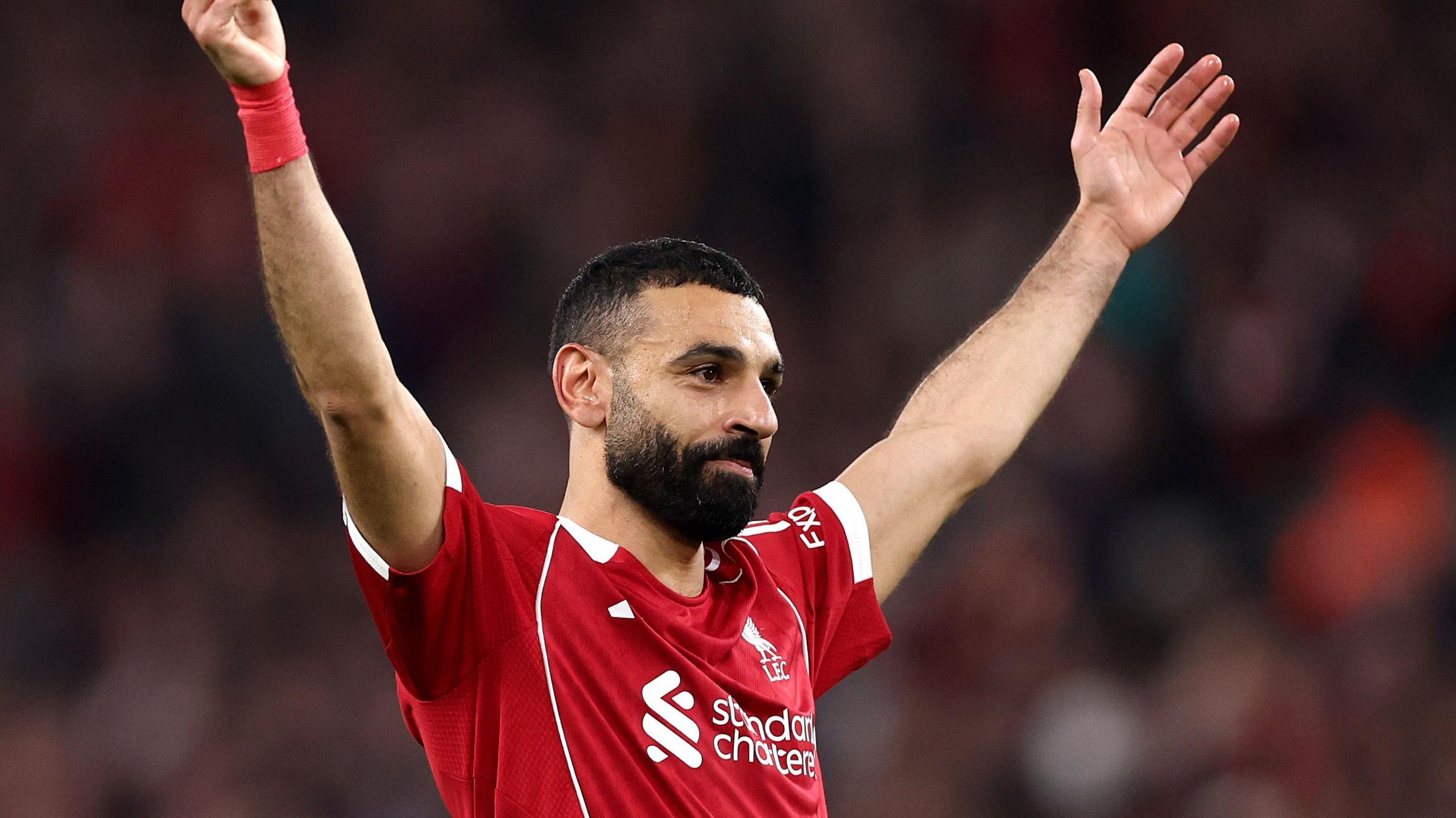 Mo Salah holds his arms up as he smiles during a Liverpool game. 