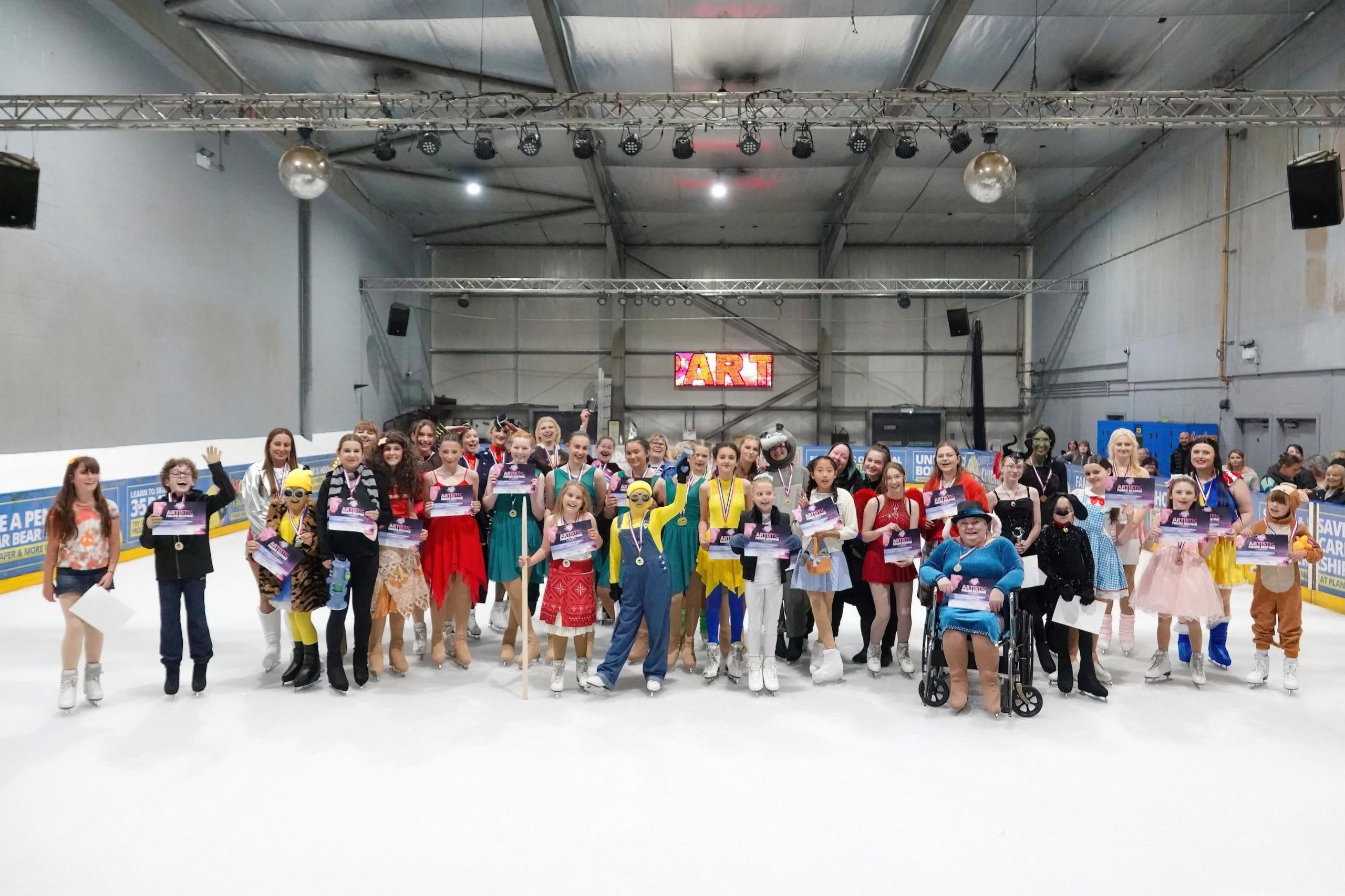 A large group of ice skaters in different costumes stand on an ice risk and smile at the camera