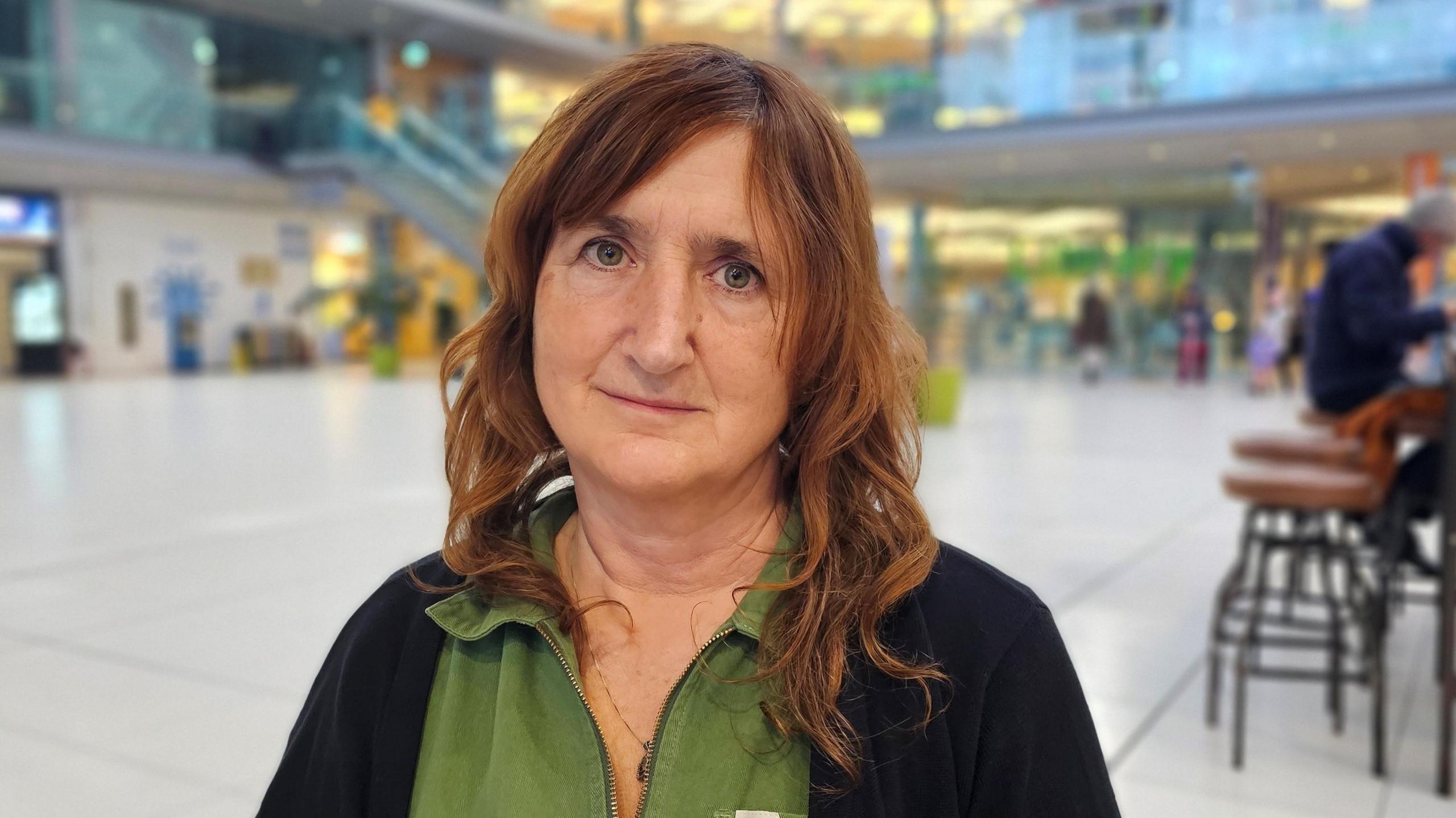 Lucy Galvin is sitting in The Forum in Norwich looking at the camera. She has a black light cardigan over a green shirt.