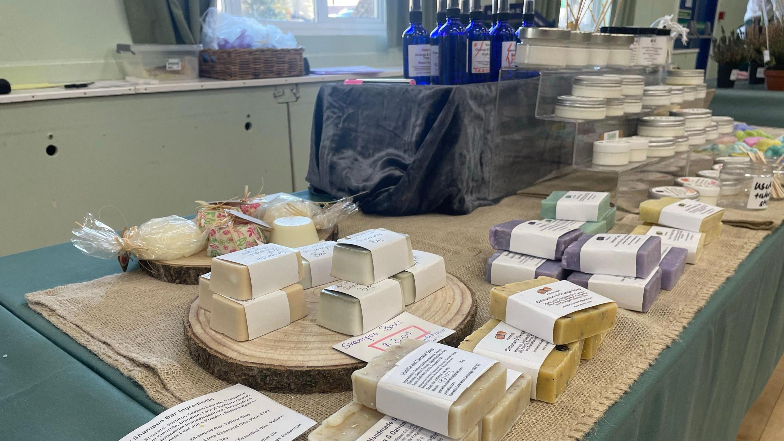 A table has lots of colourful soaps on it, as well as pots of moisturiser and blue glass jars on it.