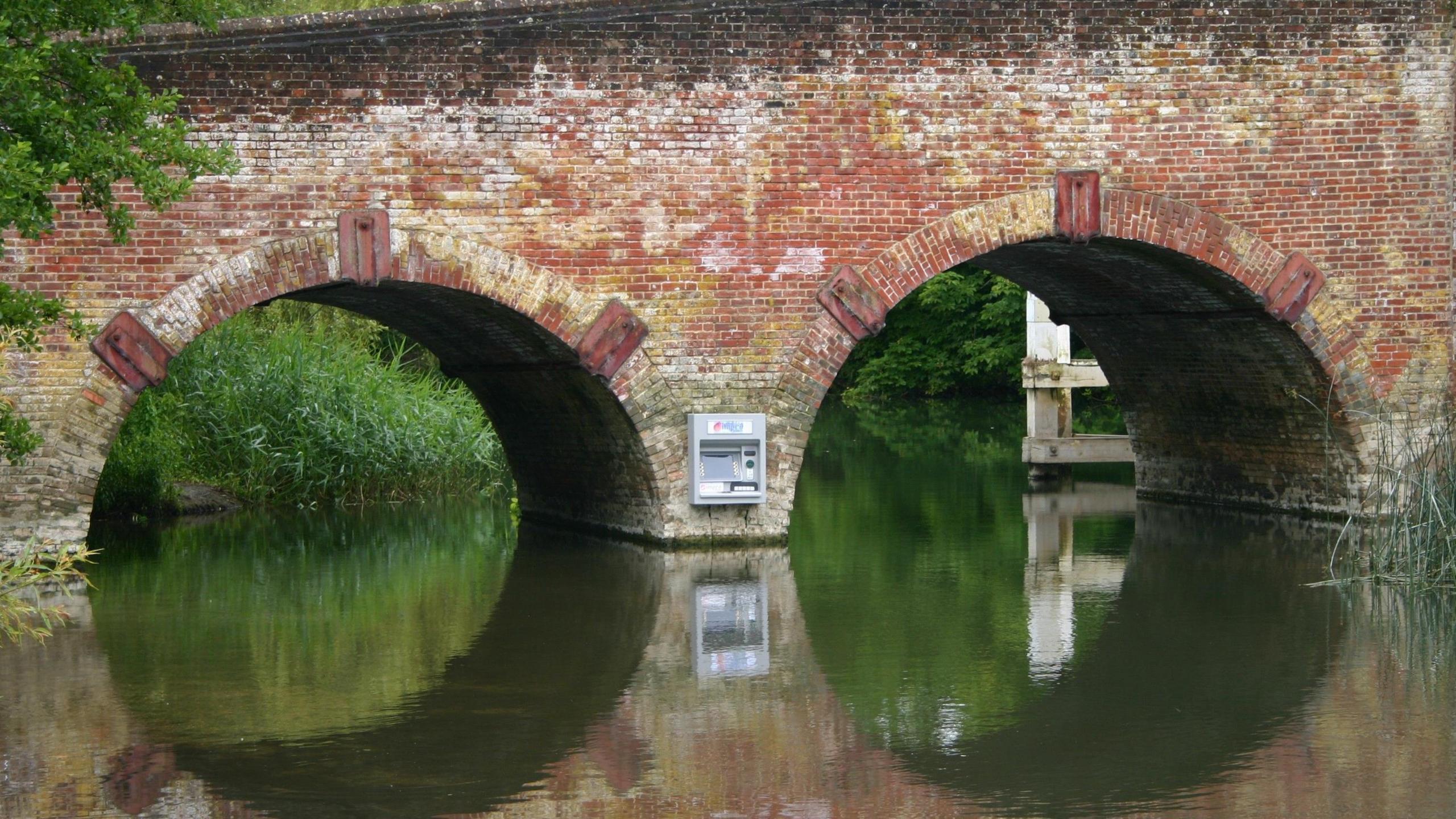 A cash machine on the side of a bridge, placed between its two arches, but inaccessible to anyone (unless they were on the river)