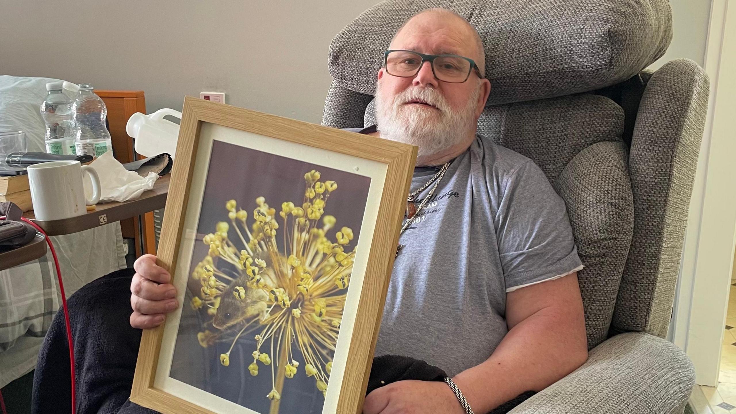 Peter Hardy holding up one of his photographs, which captured a mouse hiding inside a flower.