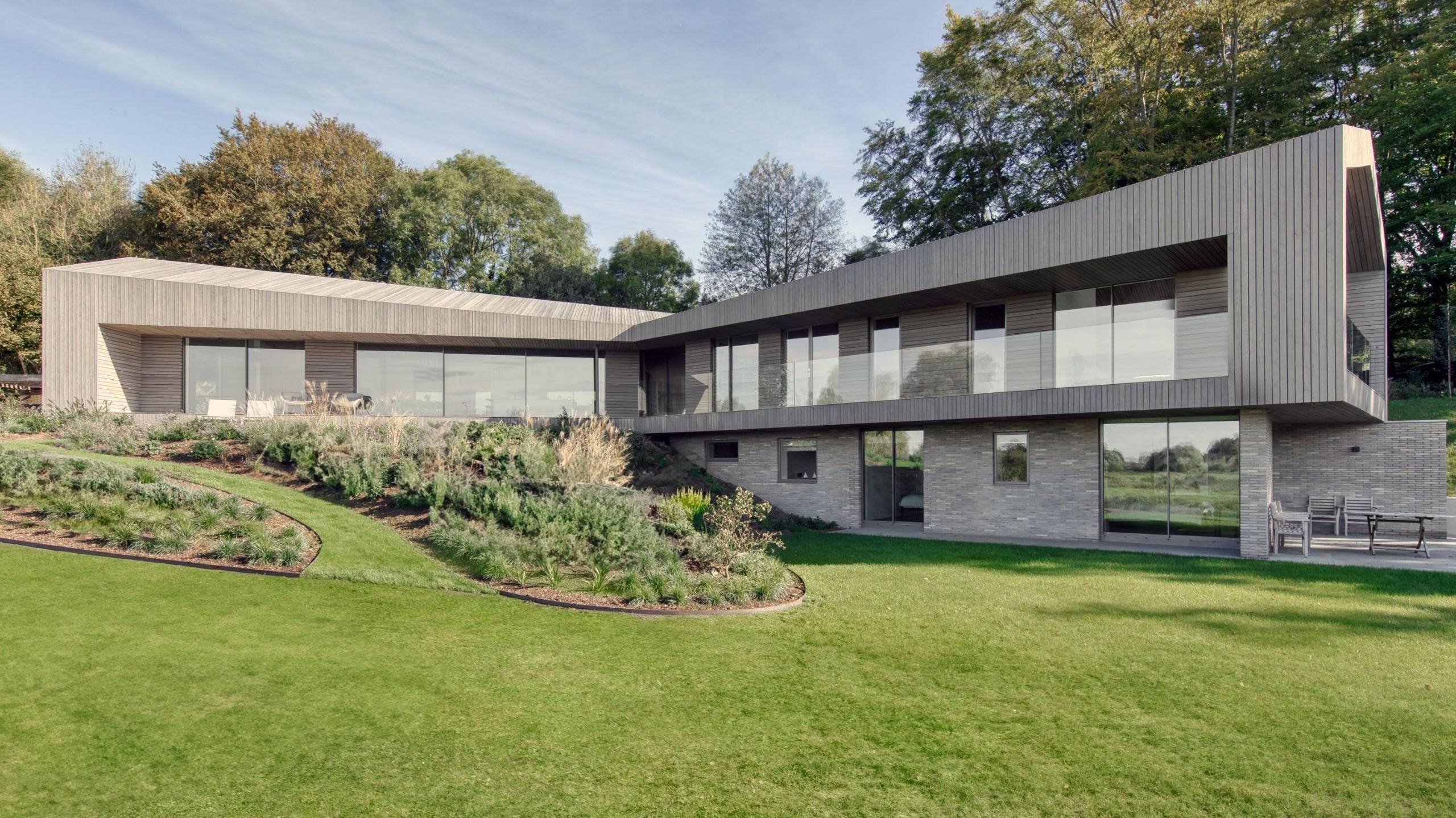 A split-level modernist house built into a bank with two visible wings at a right angle to each other with a garden and grass in the foreground 