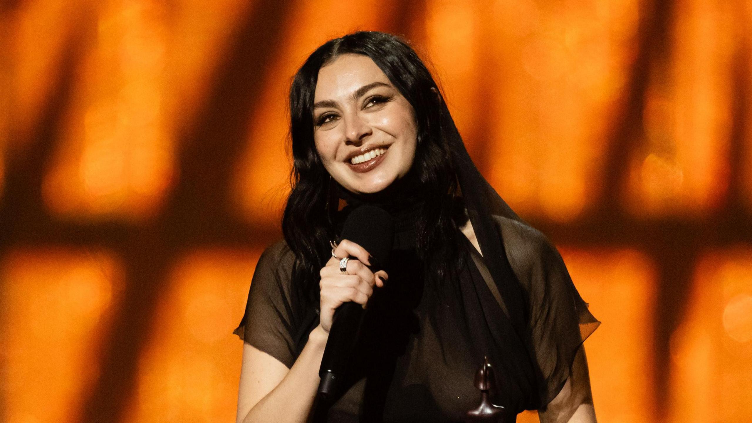 Charli XCX smiles holding microphone