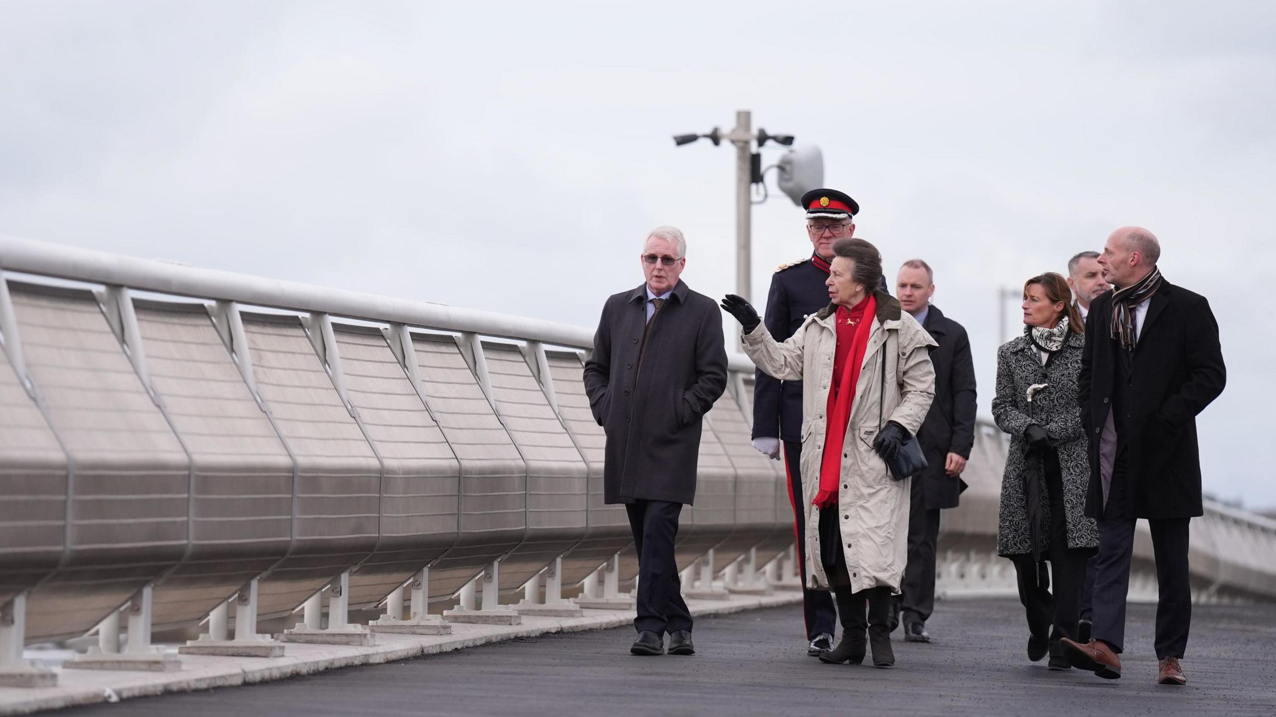 Princess Anne fronts a small group of people as they walk along Lowestoft's new Gull Wing bridge. She is talking to a gentleman next to her and using her hand to demonstrate an action.