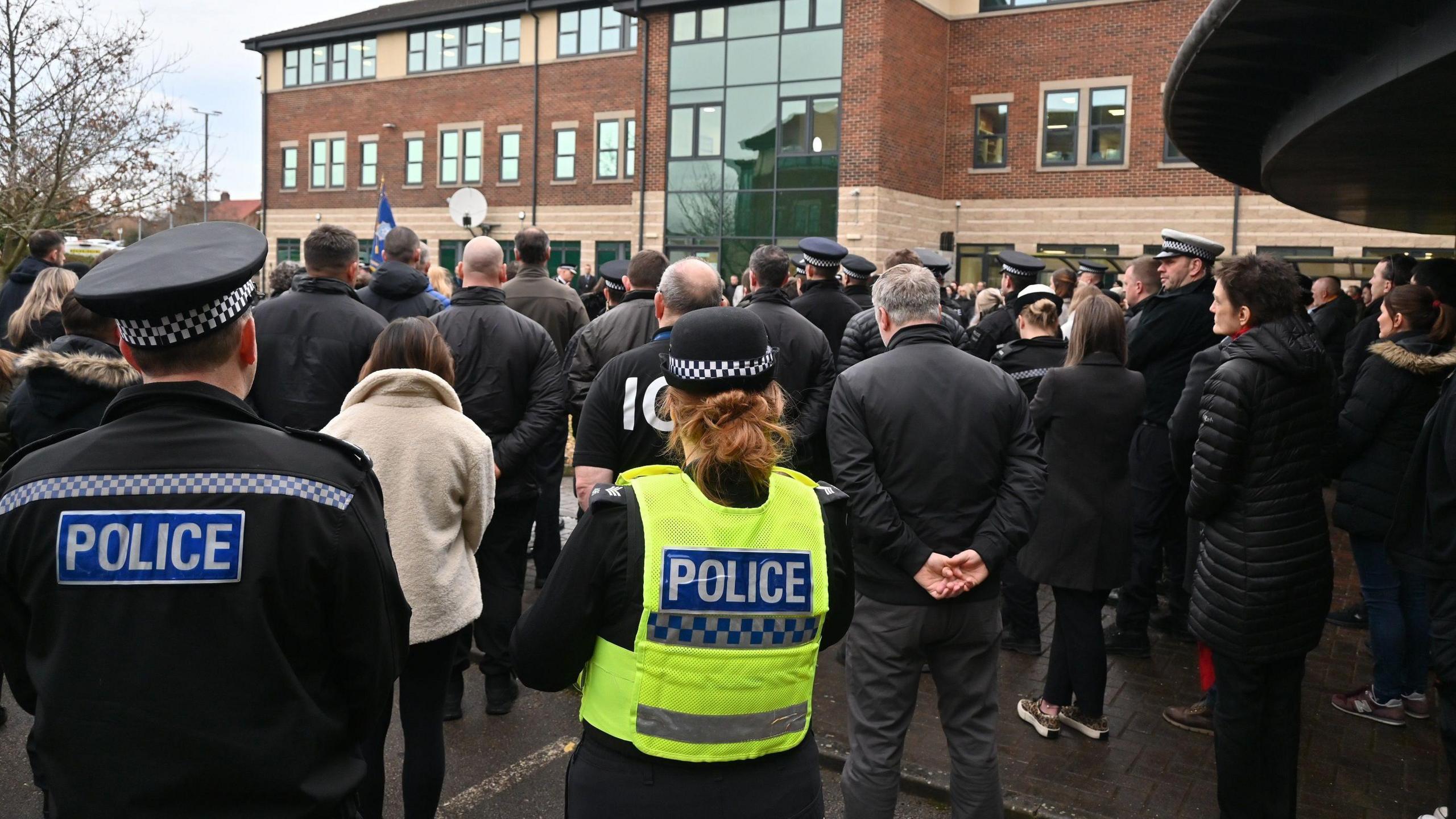 A crowd of police officers stand with hands behind their backs at a vigil outside North Yorkshire Police HQ.