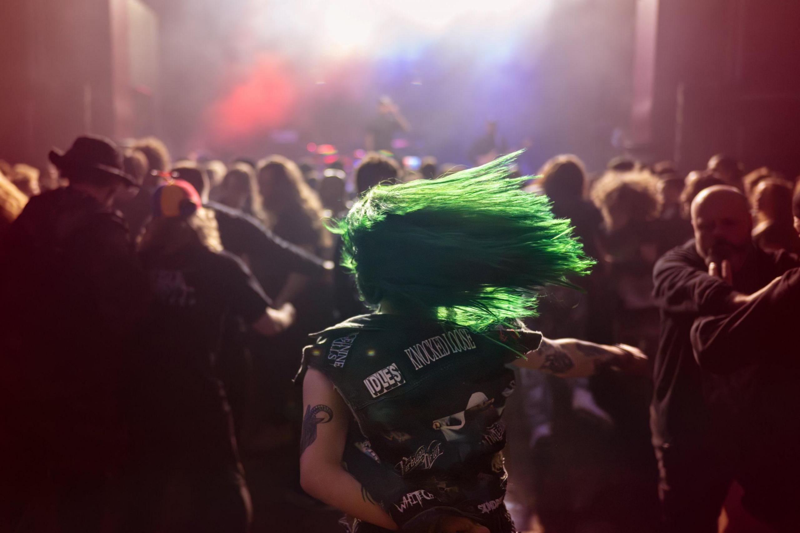 A green-haired heavy metal fan dances in the middle of a crowd