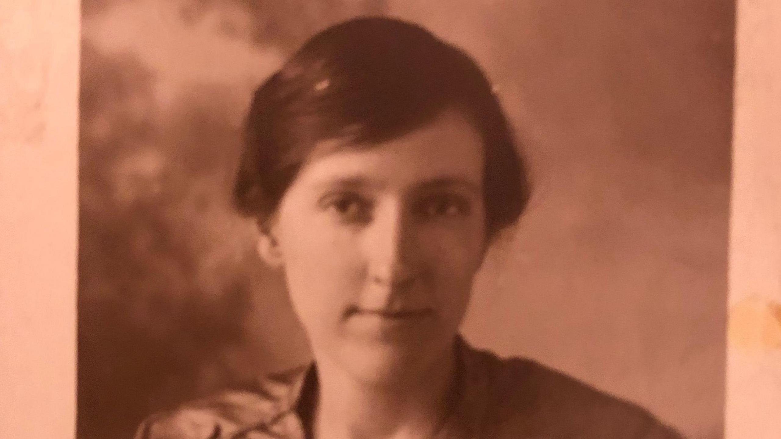 A black and white, sepia head and top of shoulders picture of Emma Marie Walton. She has short, dark hair swept across her forehead, no jewellery or make-up, and a dark coloured top can be seen across her shoulders.