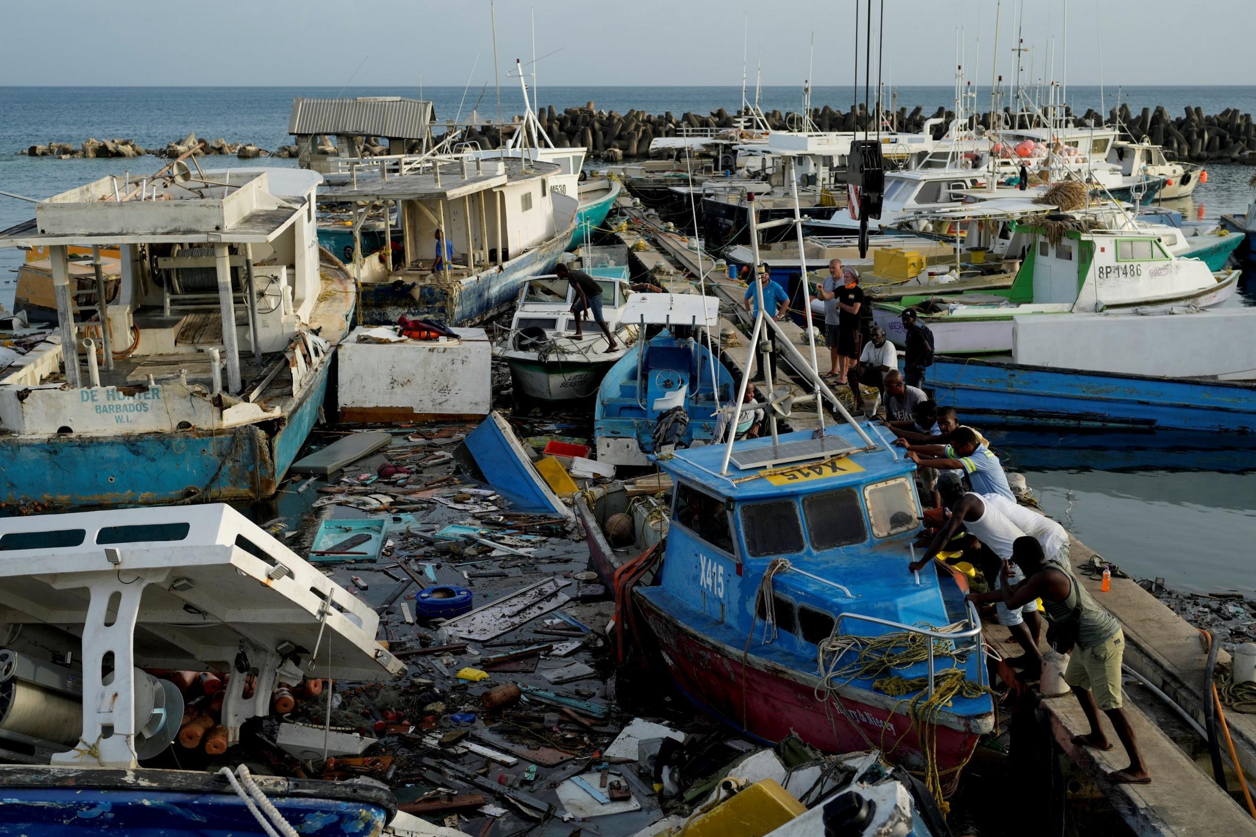 Fishermen push on a blue boat which has been pushed against the harbour wall