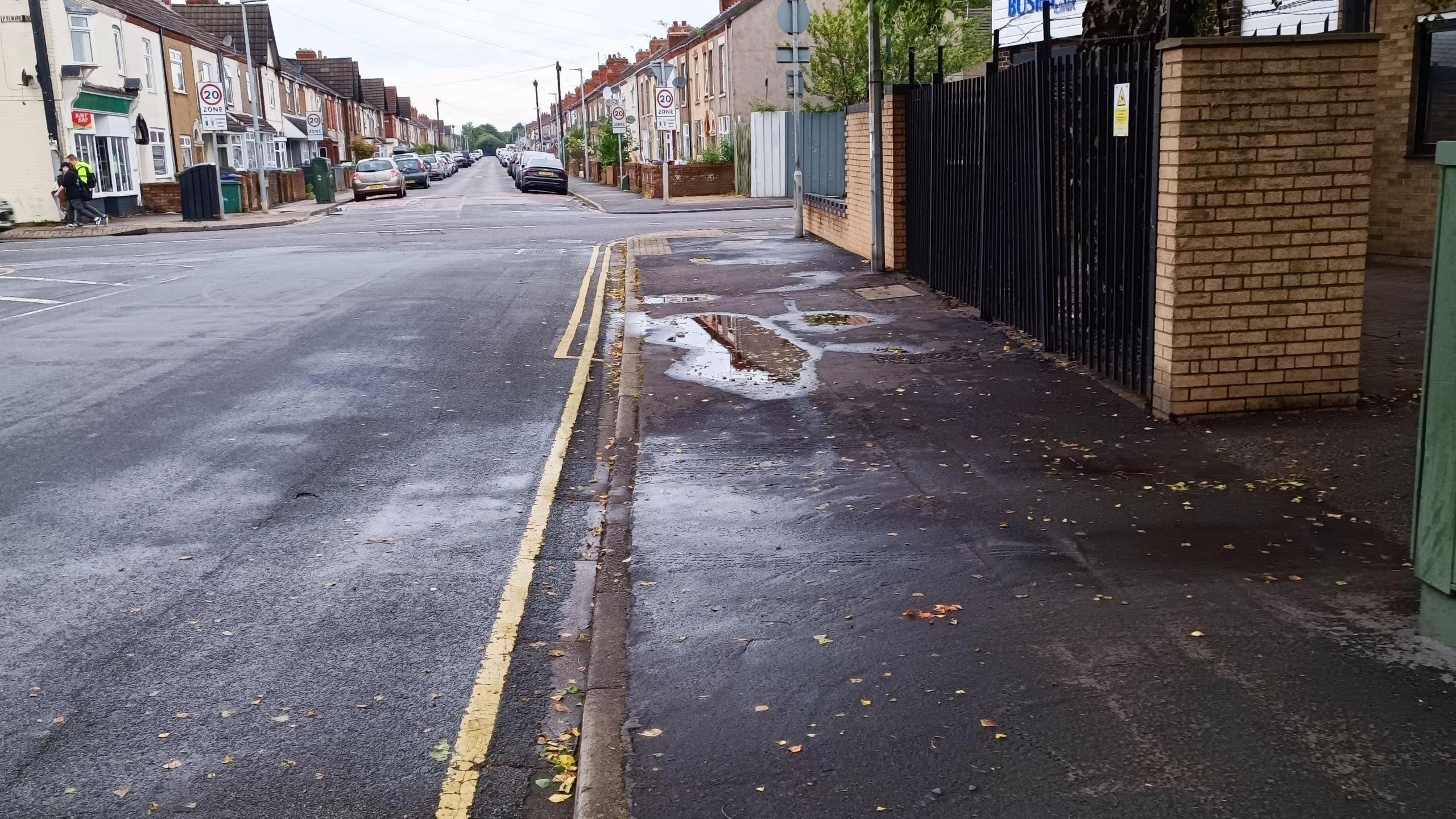 A photo of Armstrong Street showing a road with yellow road markings and a path. In the distance are residential houses with cars parked on the street.