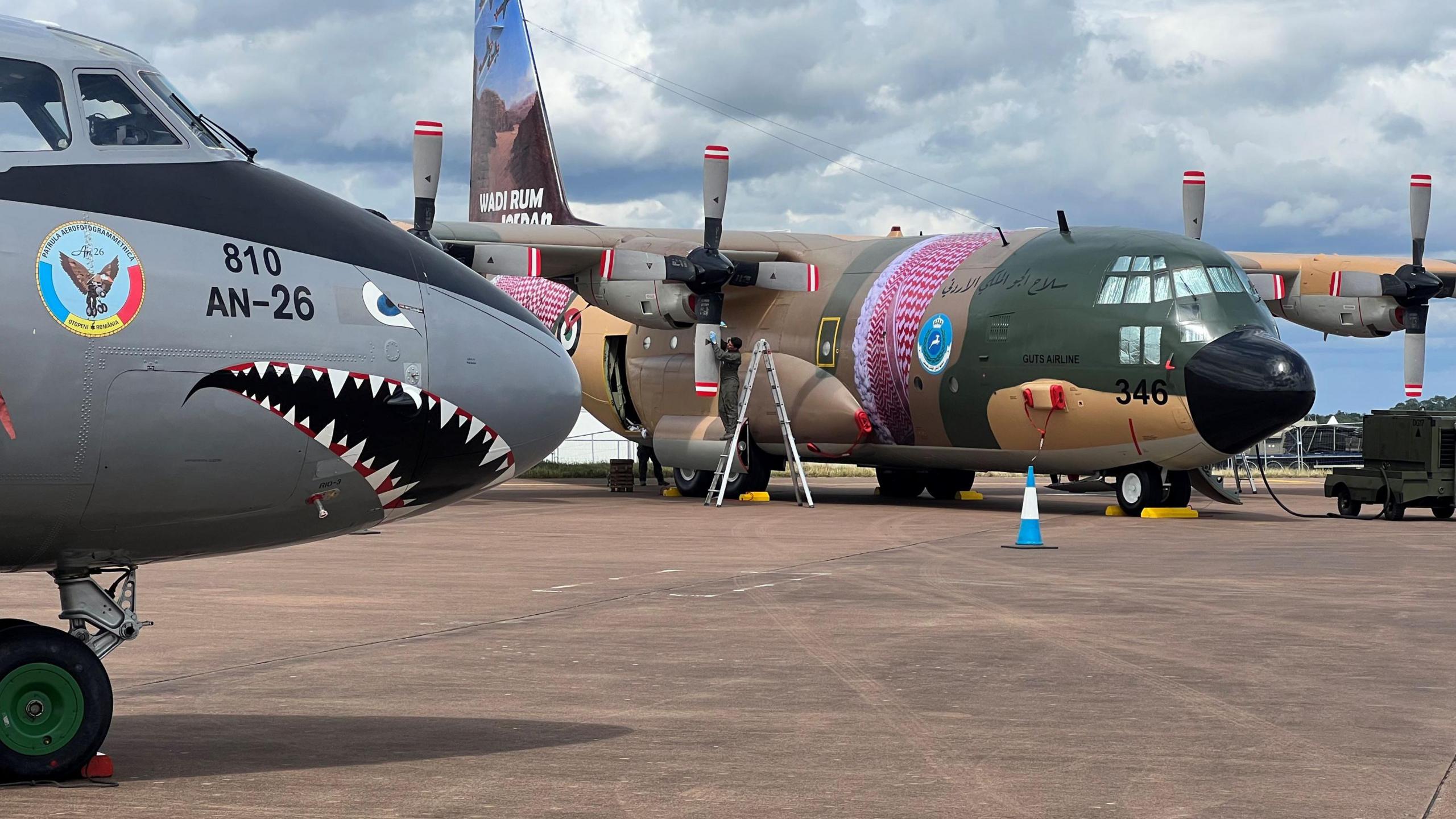 Two planes, one has a shark face painted on its nose, the other is green, brown and pink