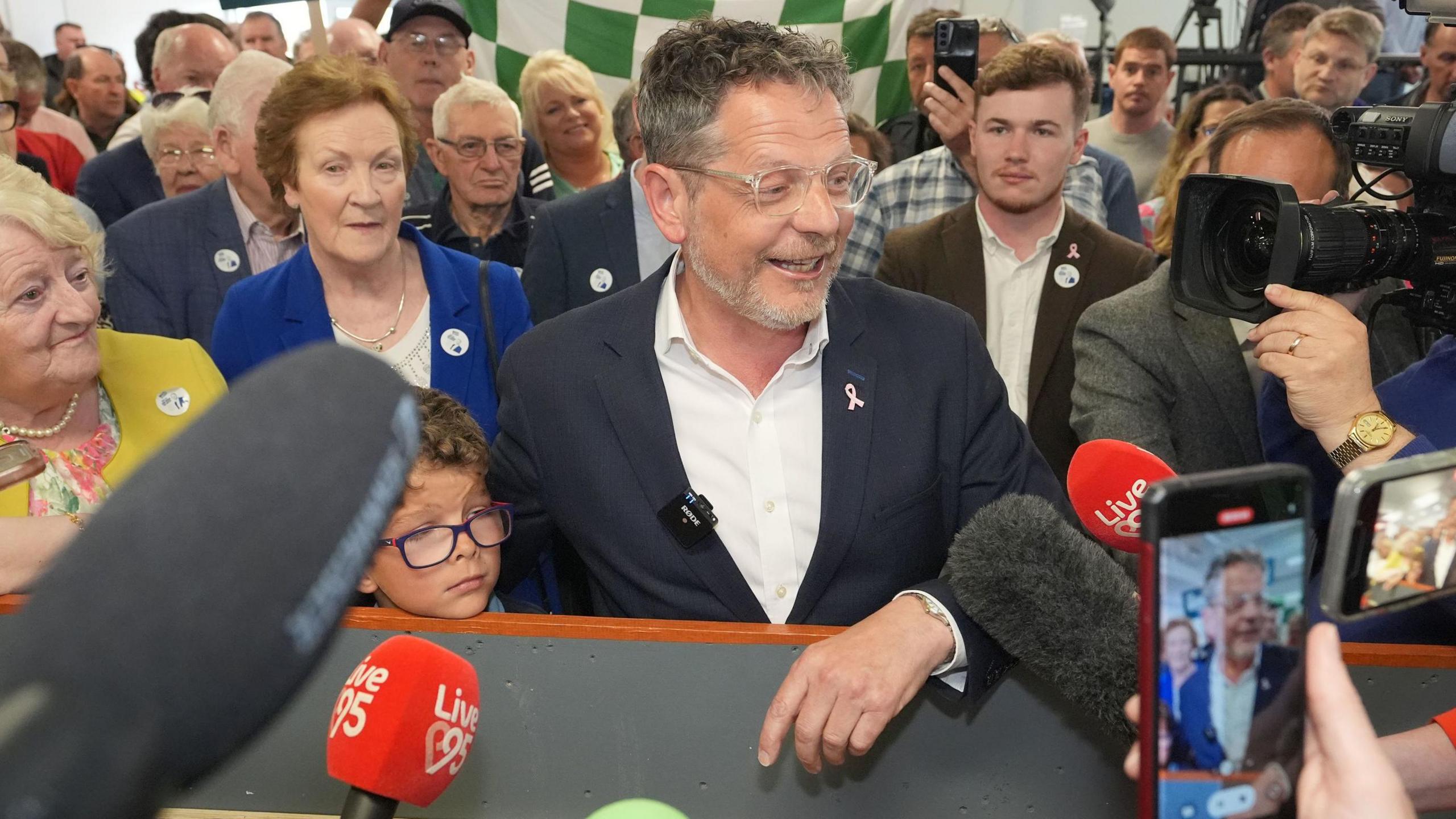 John Moran surrounded by people, mics and cameras