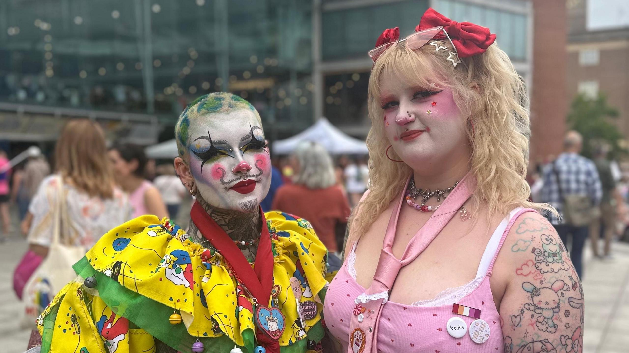 River, who is on the left, is wearing a yellow and green clown costume and has face paint on. On the right is Bláz who is wearing a pink outfit with a tie.
