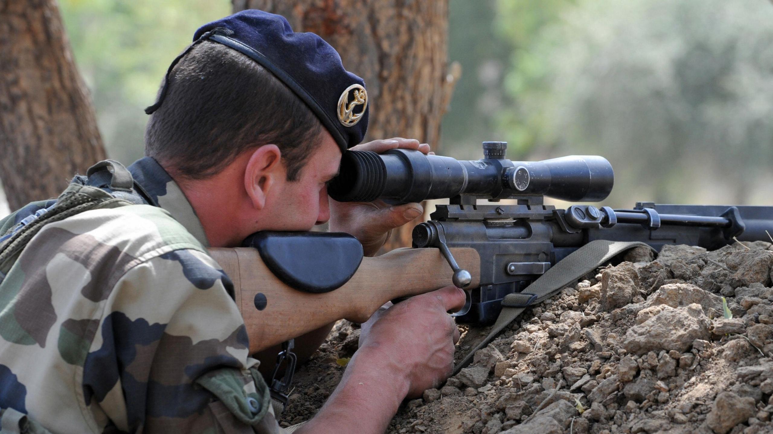 A French soldier in military fatigues looks through his rifle with a finger on the gun's trigger.