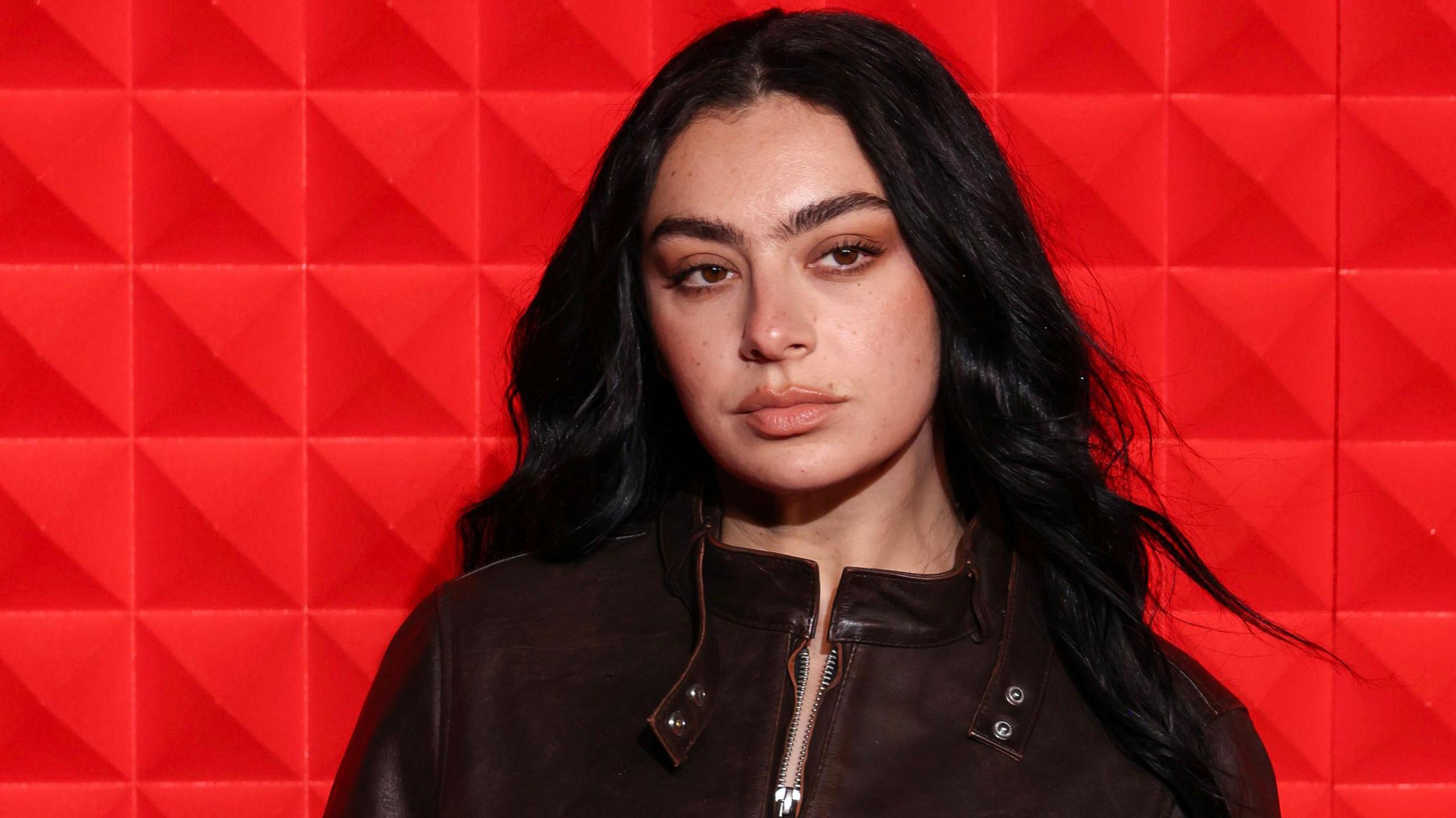 Charli XCX poses against a red background