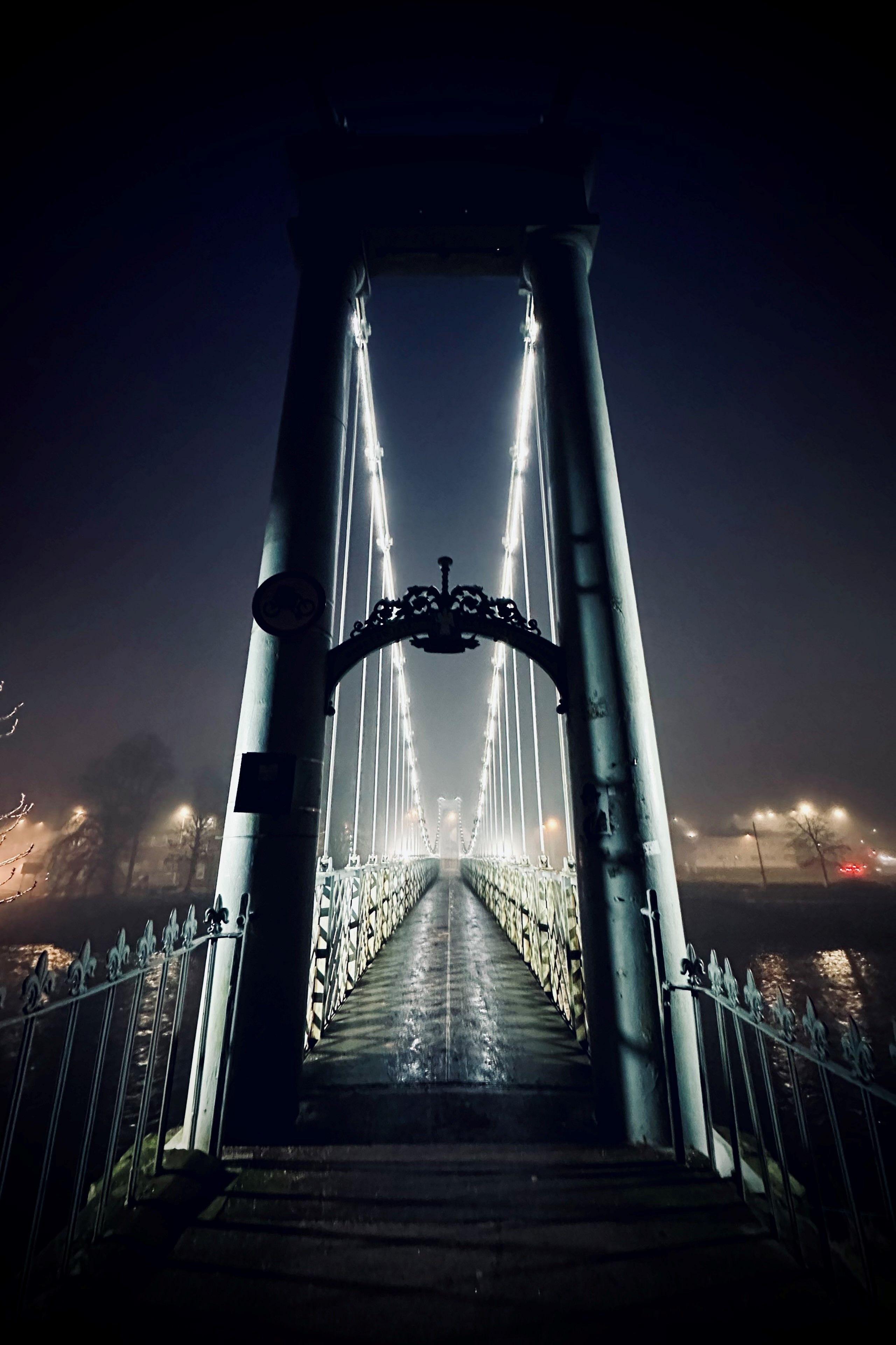 A set of lights strung across a bridge on a misty morning while the sky is still dark