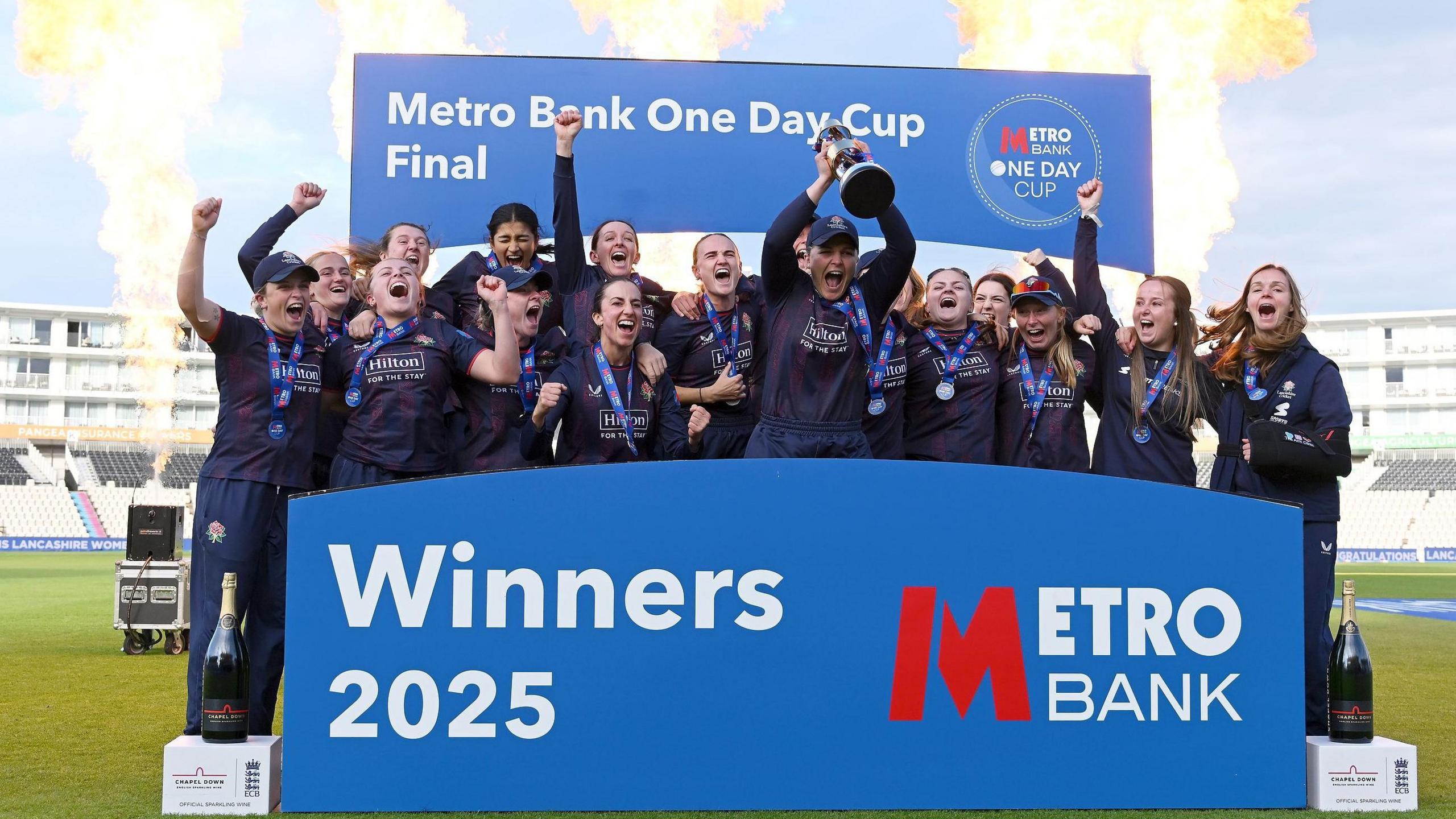 Lancashire captain Ellie Threlkeld lifts the One-Day Cup trophy along with her team-mates on the podium  