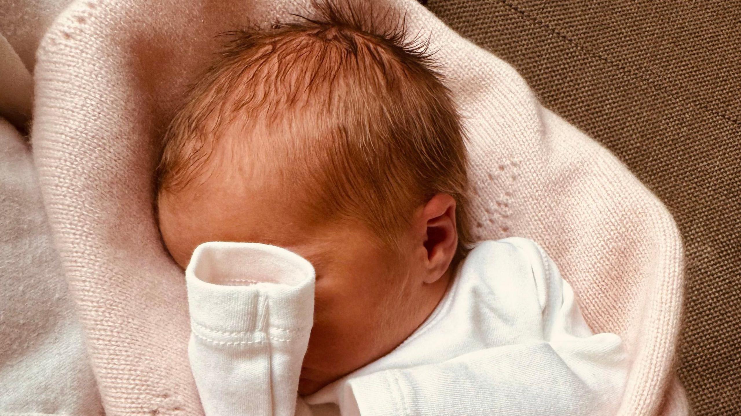 Baby girl Athena is pictured in a close-up photograph showing most of her head, with her hand covering much of her face. 