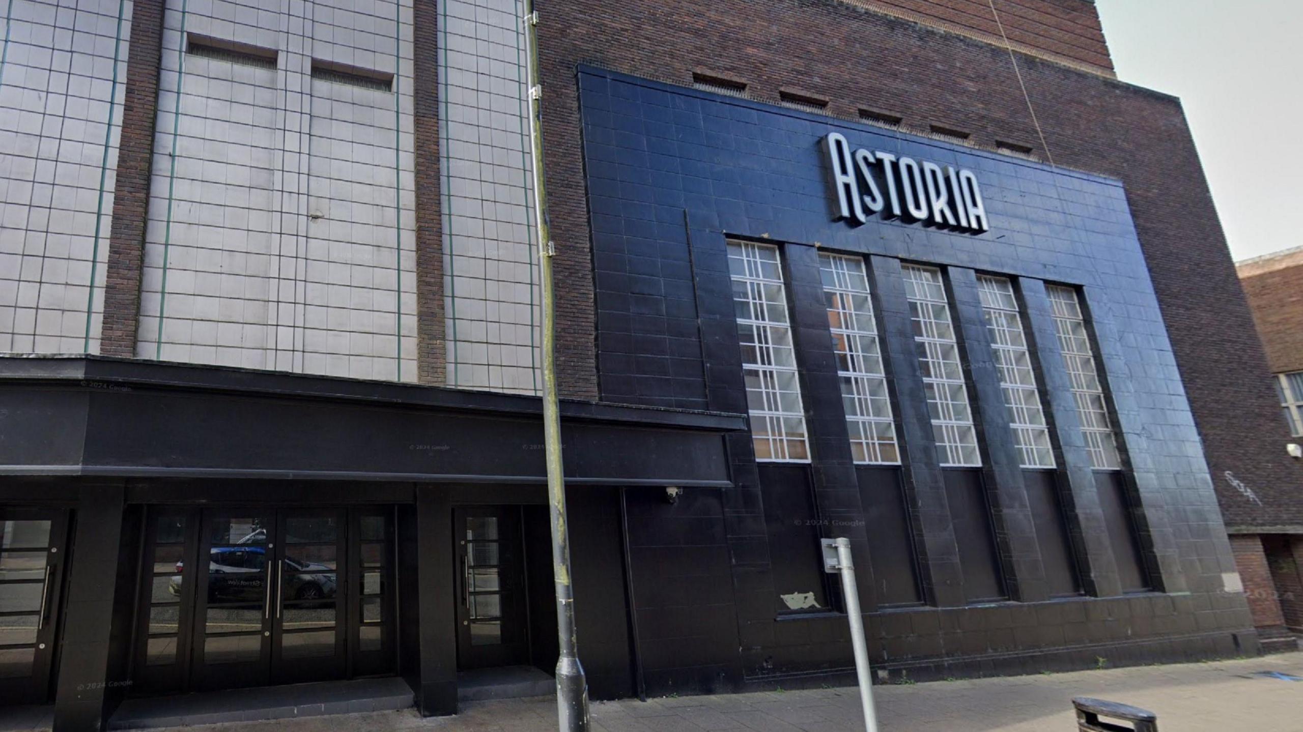 Outside of a music venue with brown and white bricks. The right of the building is painted dark blue with the word ASTORIA in silver lettering on a sign