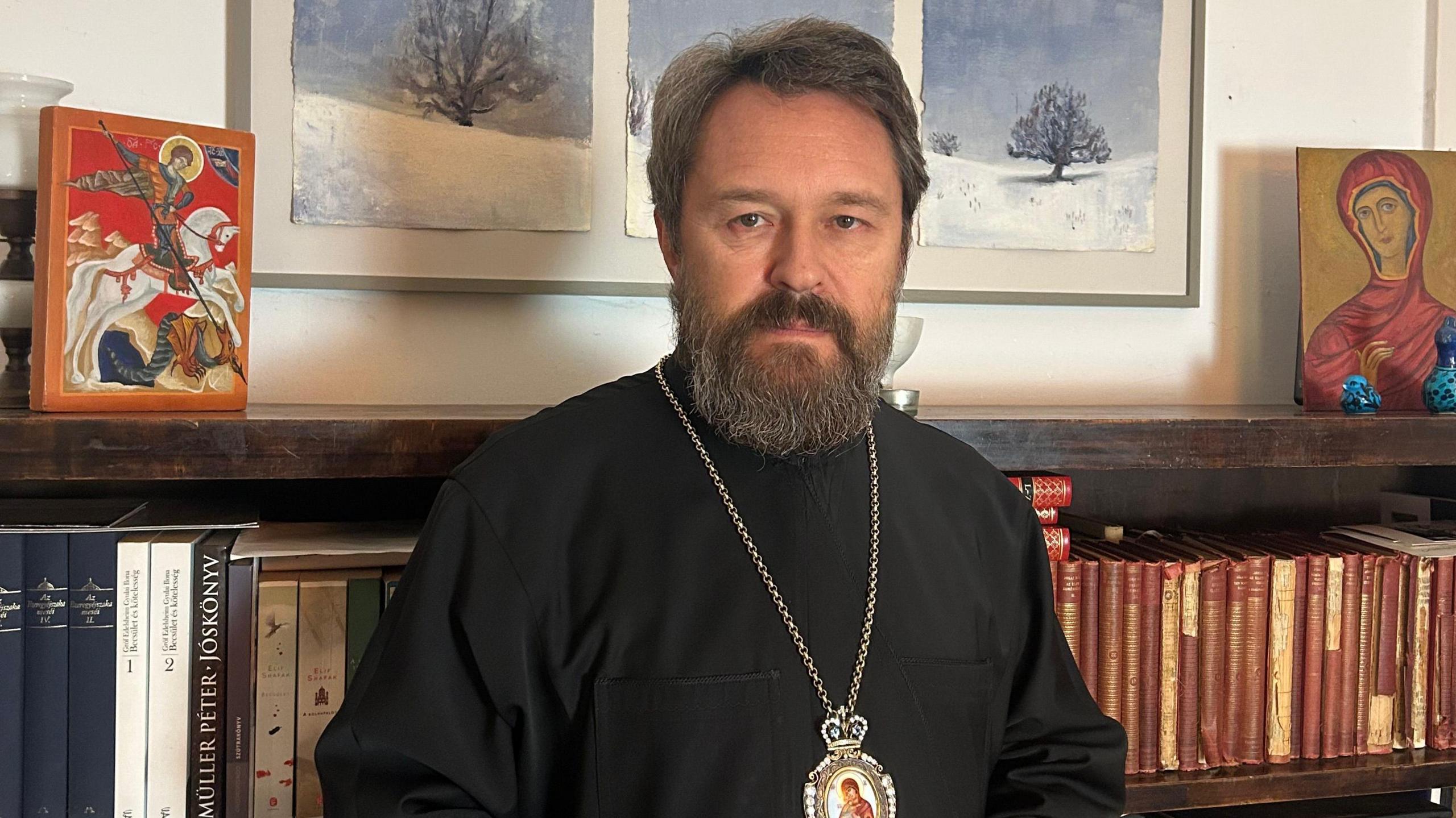 Metropolitan Hilarion stands in front of a bookcase in Budapest