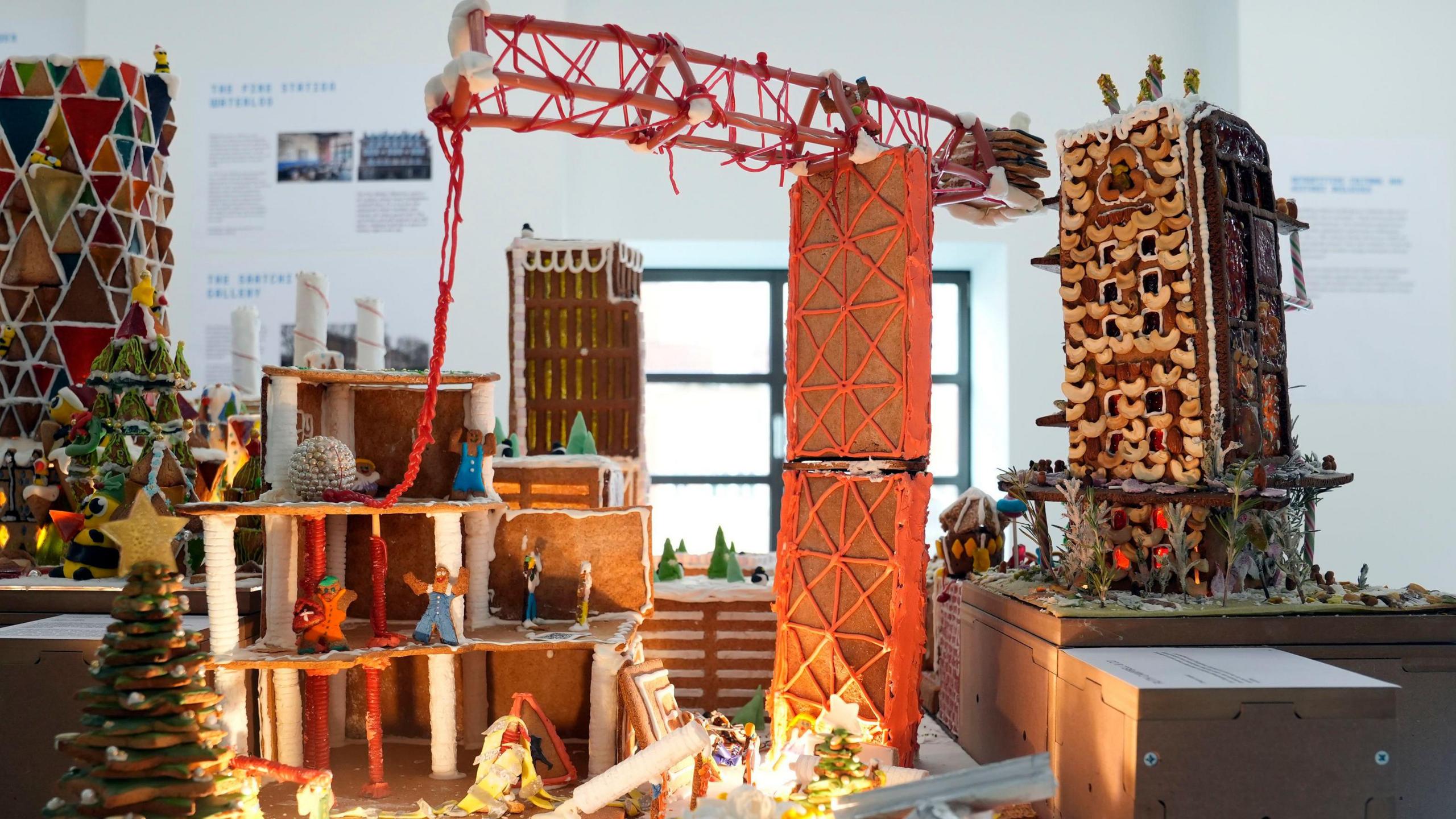 A construction site with a gingerbread crane and a building under construction. Workpeople are depicted waving their arms in a manner that would be unsafe if it was real.