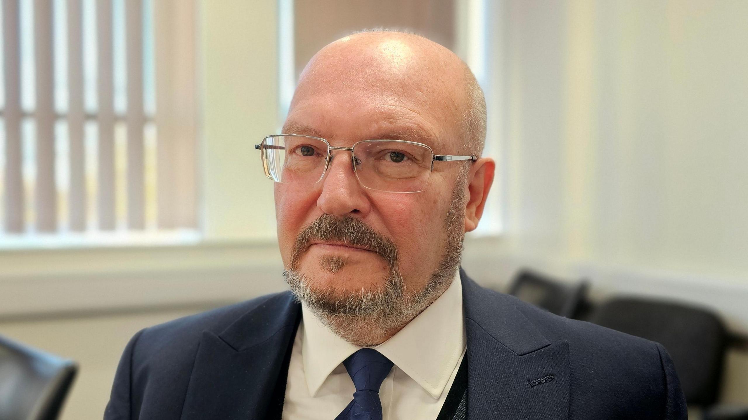 Graham Plant wearing glasses and a blue suit jacket, with blue tie and white shirt.