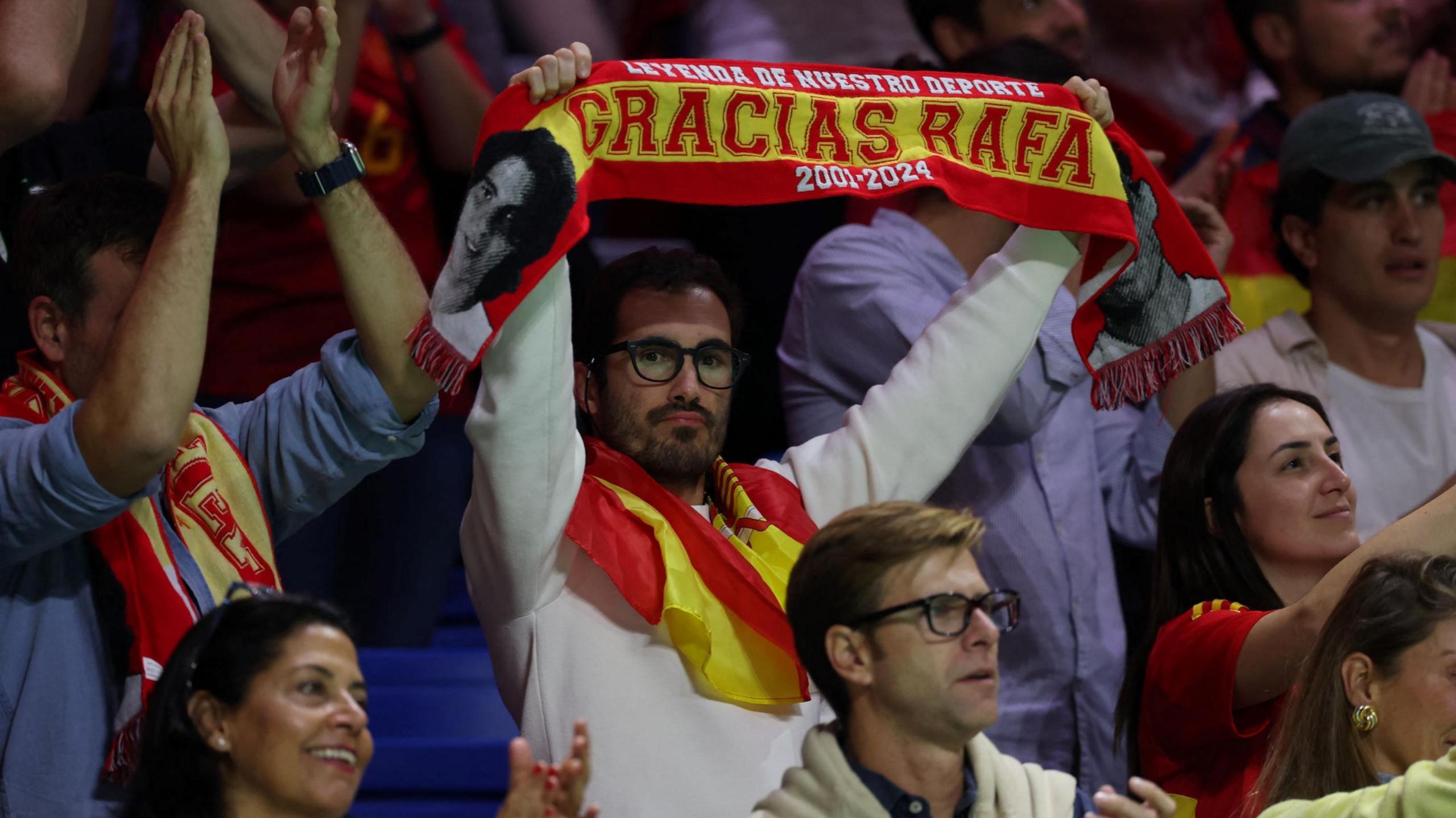 A Spanish fan holds up a scarf which says 'Gracias Rafa'