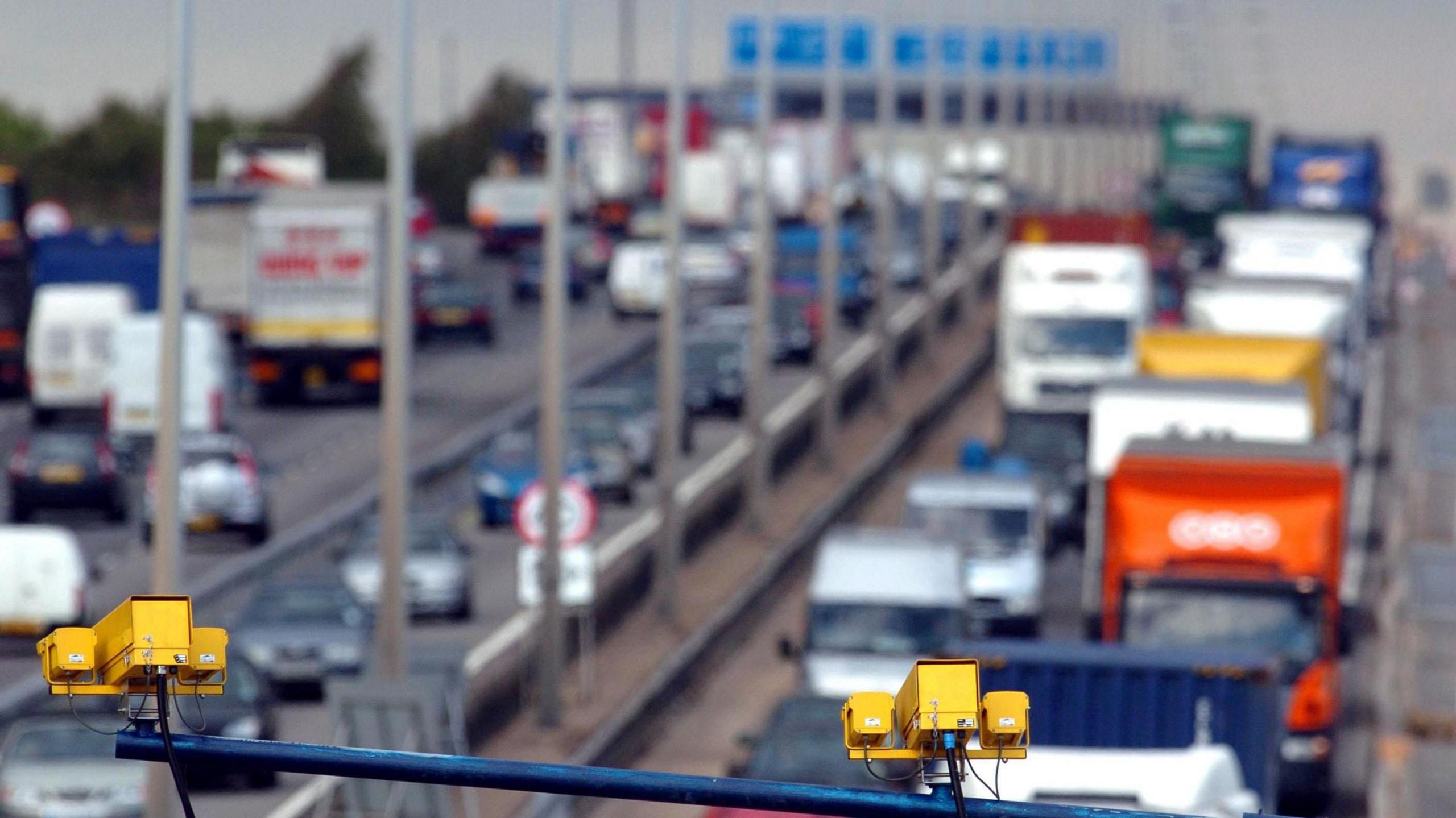 Queueing traffic on the M1 in Hertfordshire near junction nine. There is blue signage and yellow average speed cameras visible