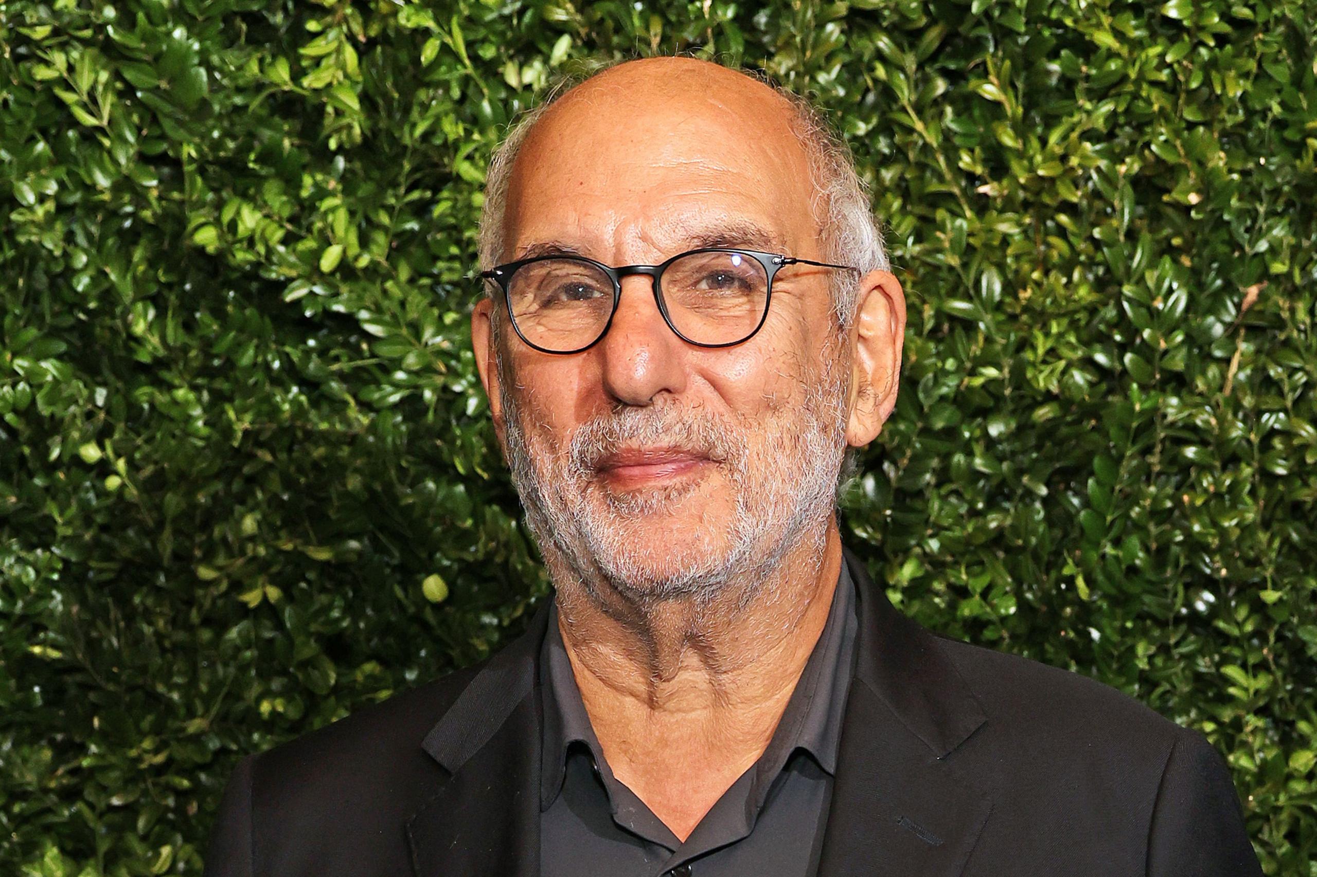 Alan Yentob ka veshur një këmishë të zezë me jakë të lidhur me një xhaketë të zezë. Sfondi përbëhet nga një mur i dendur jeshil me gjethe, duke krijuar një sfond natyral dhe të gjallë. Ndriçimi është i njëtrajtshëm, duke nxjerrë në pah teksturën e gjelbërimit dhe veshjet e errëta.