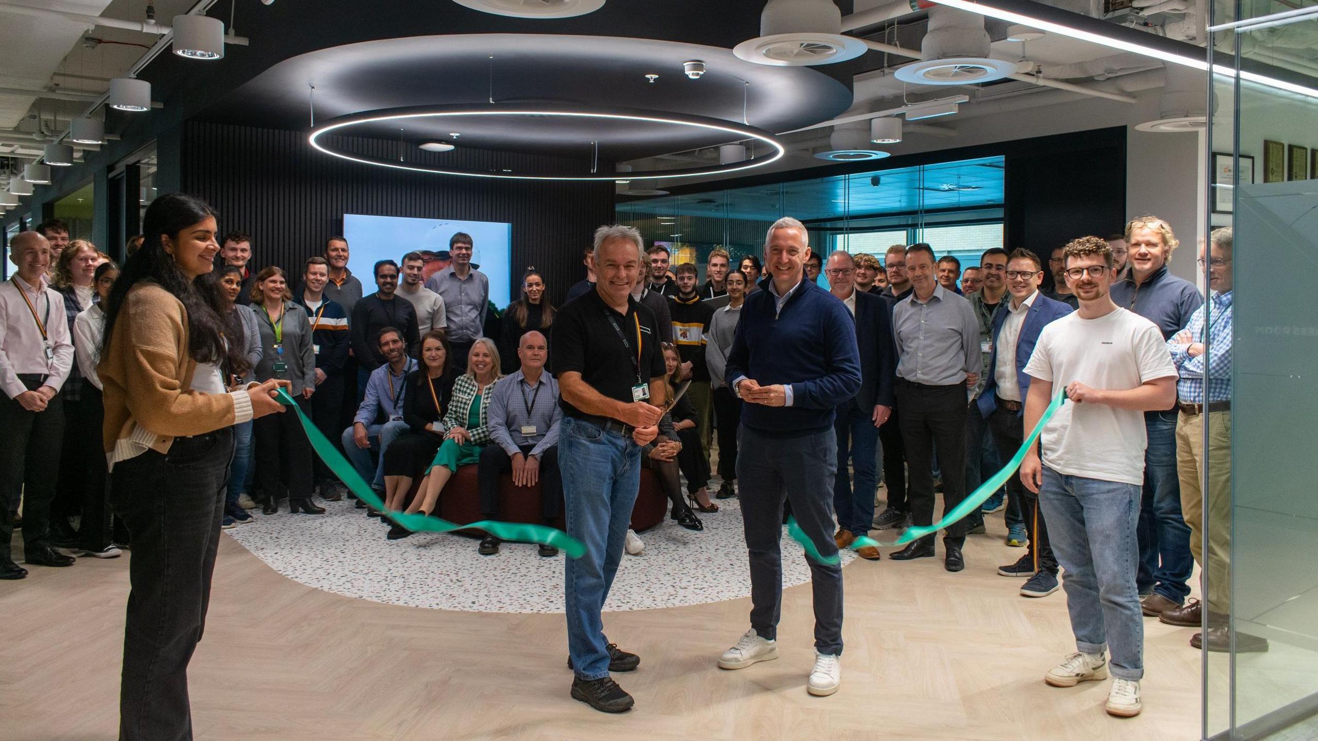 A large group of employees are grouped together facing the camera as a ribbon is cut to mark the opening of new Hewlett Packard offices in Bristol. Glimpses of the modern office are visible in the background