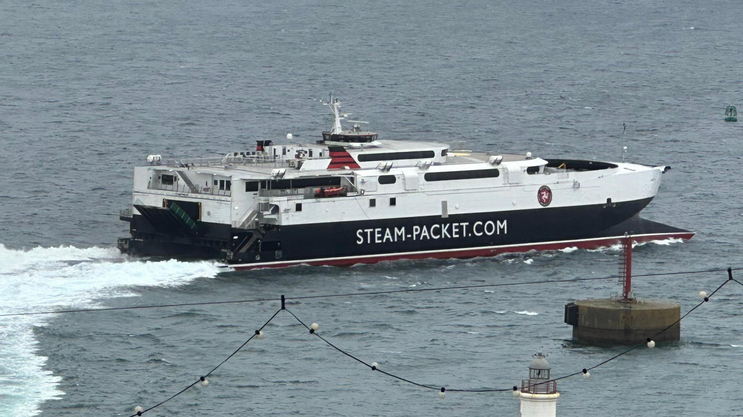 The fast craft Manannan sailing out of Douglas Harbour. It is white, black and red and had STEMA-PACKET.COM written on the said.