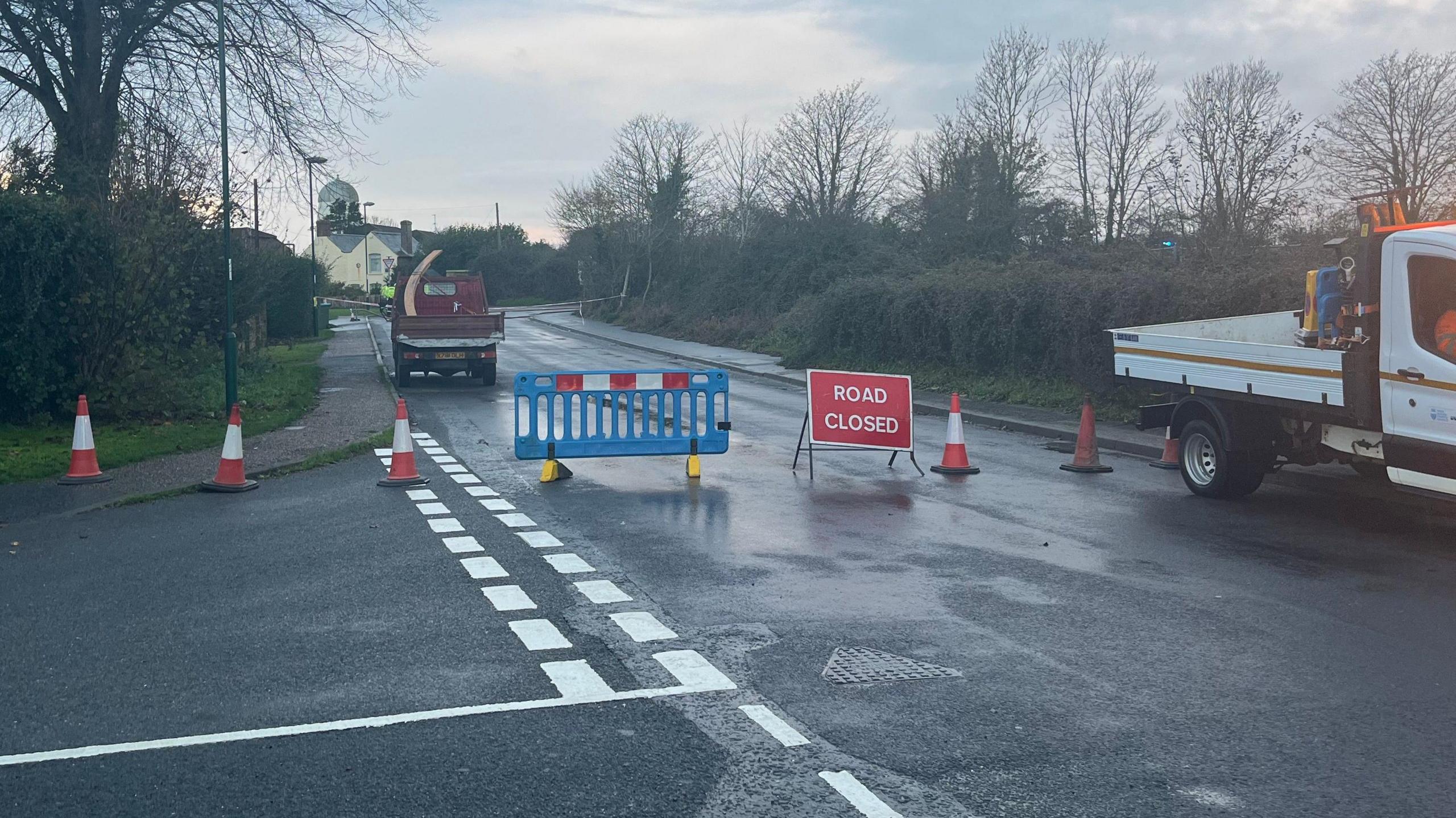 A sign advising that the road is closed on Pagham Road, near Nyetimber, West Sussex, where a car crashed into a gas substation. Several cones are set out on the road.