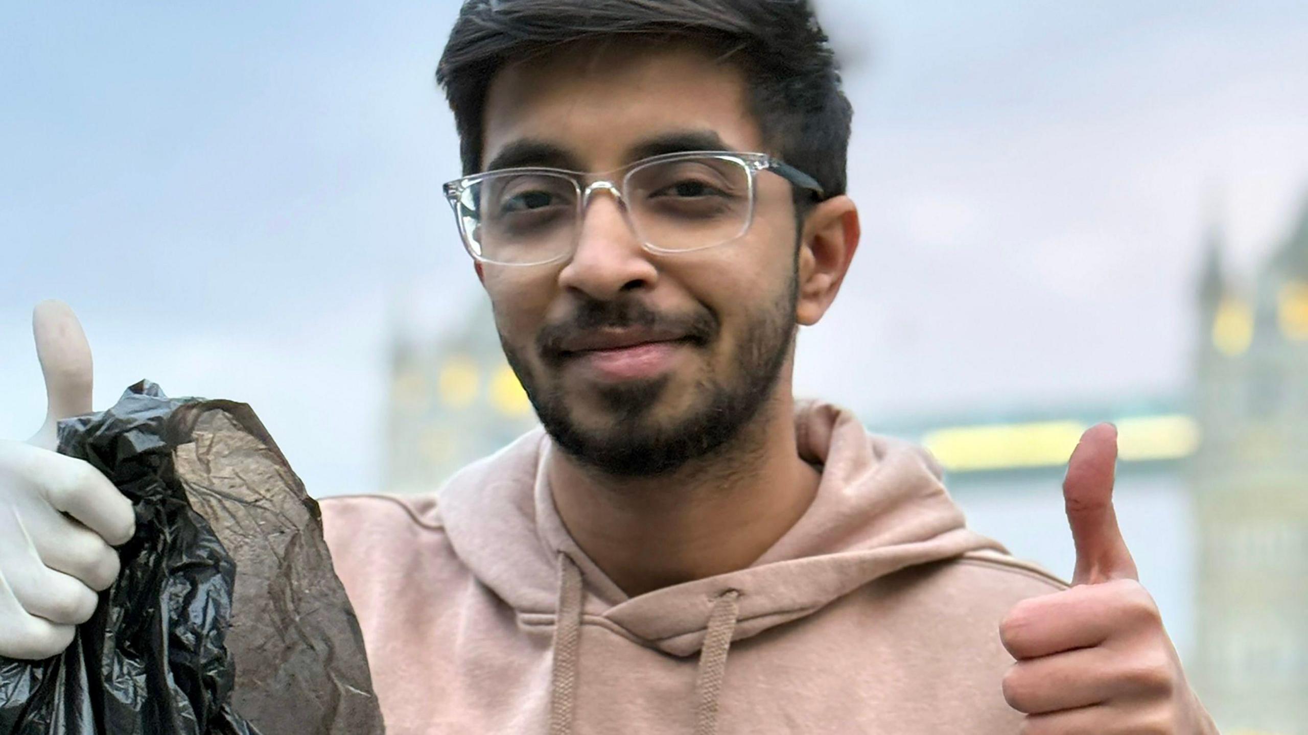 Vivek holds his thumbs up whilst holding a black bin liner 