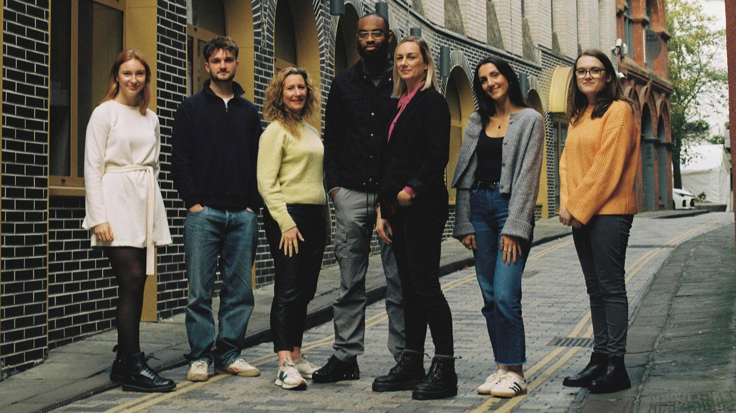 A group of five people, two men and five women, from the Bristol company Purplefish, stand in a line in a small street, wearing casual clothes, and facing the camera.