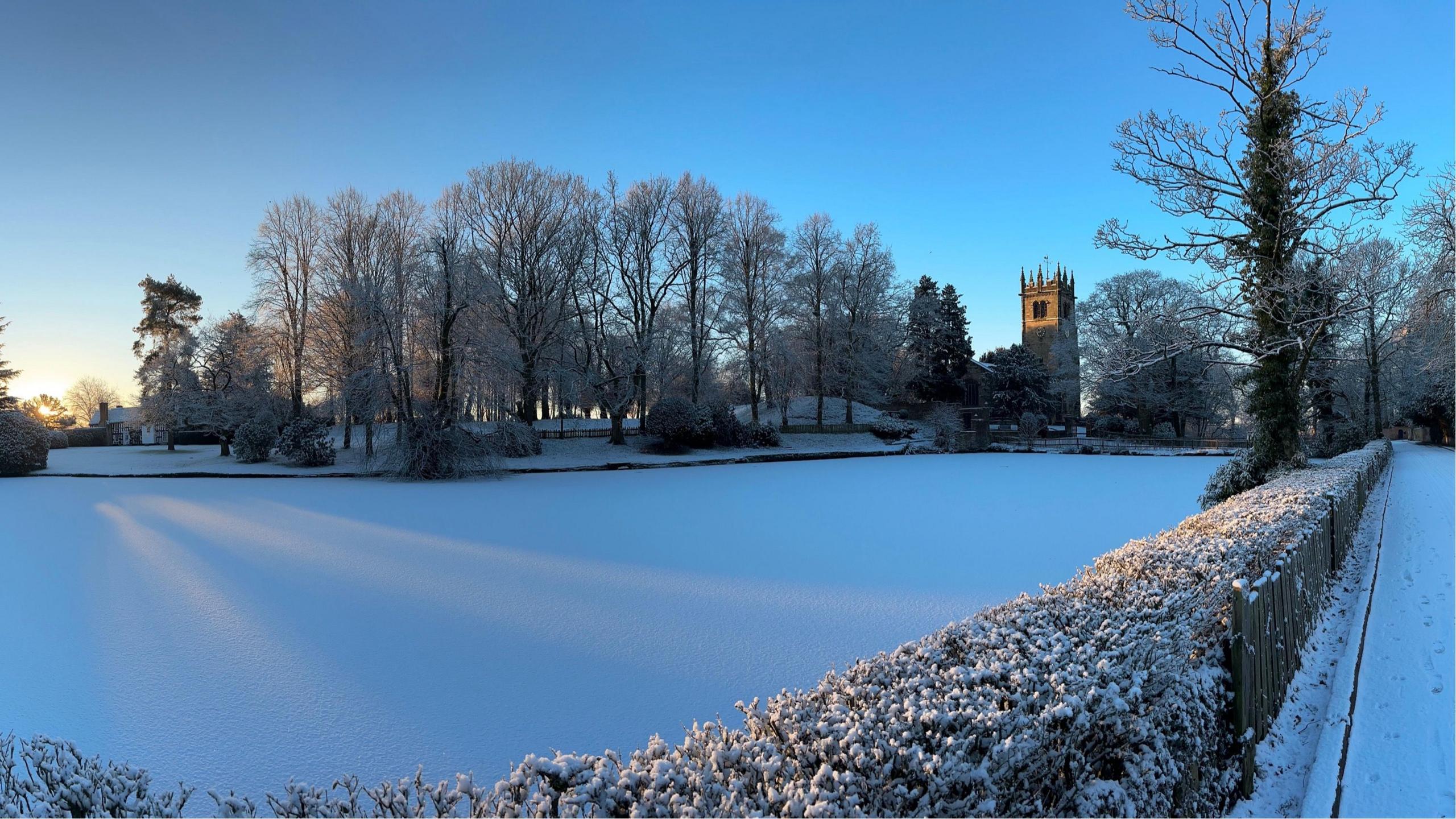 Snow-covered land in front of a church, with blue skies overhead