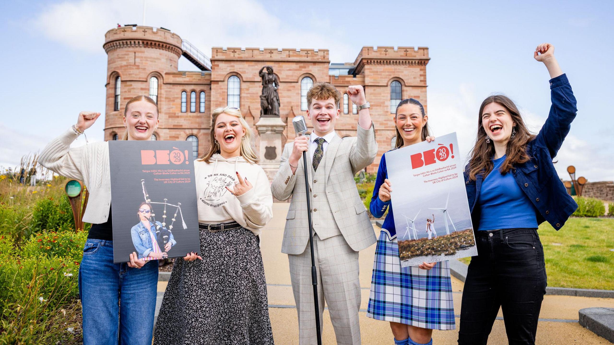 Ceathrar bhoireannach òg agus gille - aig cuirm a' comharrachadh gu bheil tagradh Inbhir Nis airson a dhol na Chathair-bhaile a' Chultair air a chur a-steach gu foirmeil. Tha iad a' cumail sanasan le ainm an tagraidh, BEÒ, sgrìobhte air, agus tha coltas gu math toilichte orra uile. 