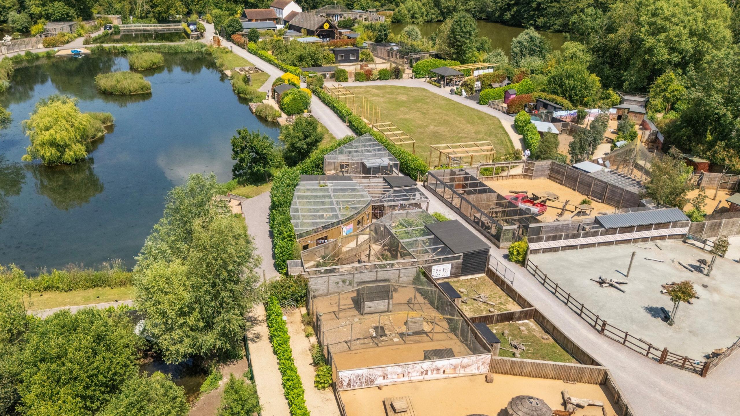 An aerial view of a farm with a number of small enclosures, trees and a lake