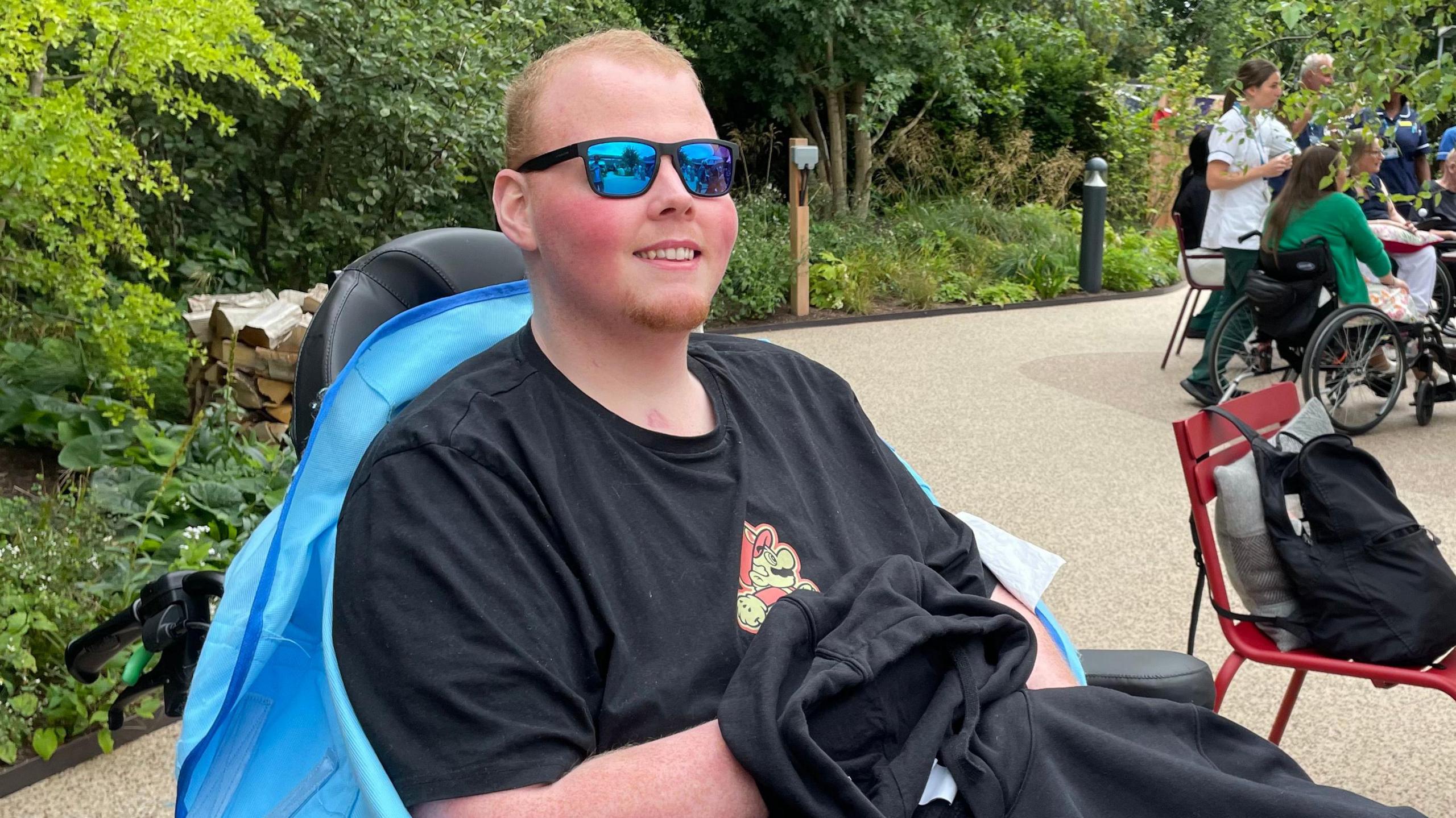 James Hunter, a young man wearing a pair of blue reflecting sunglasses, sat in his wheelchair in the garden.